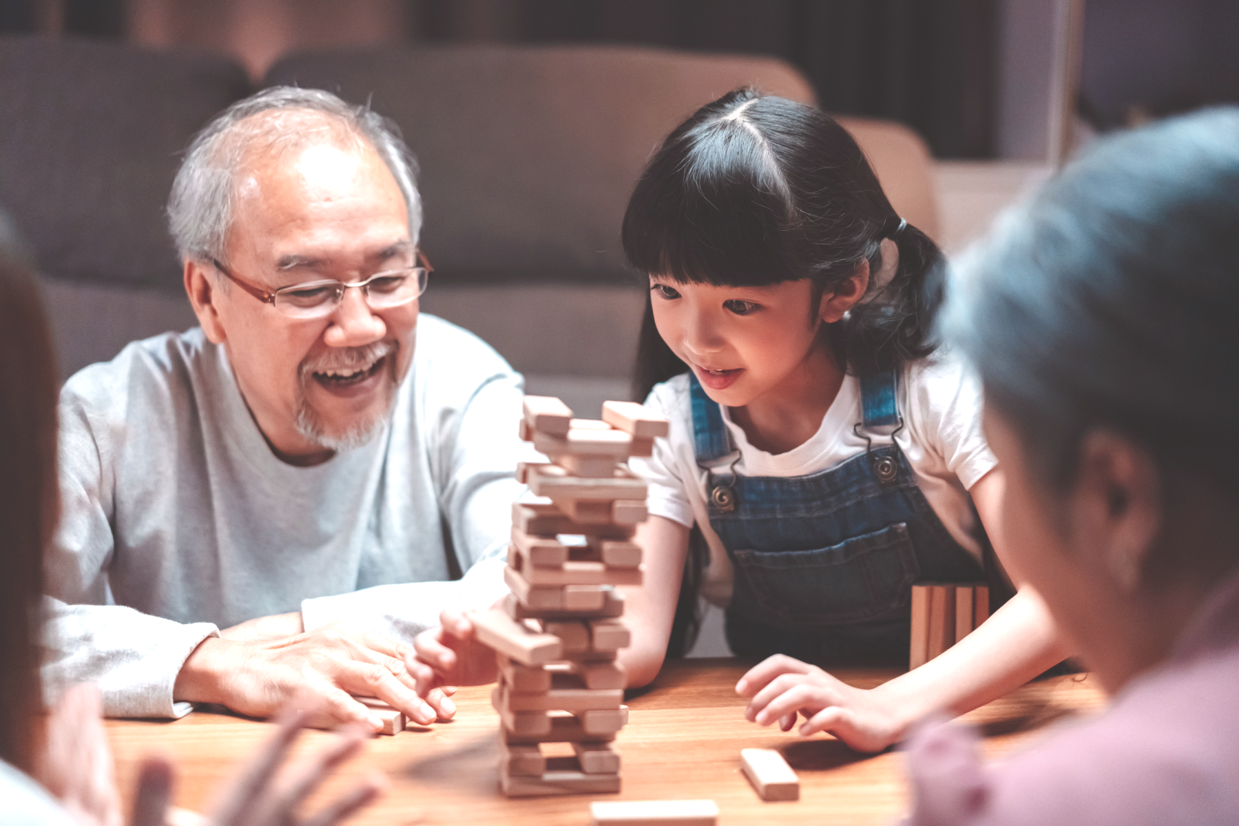 Children and an elderly man playing a game of Jenga together at a table, enjoying the game and each other's company.