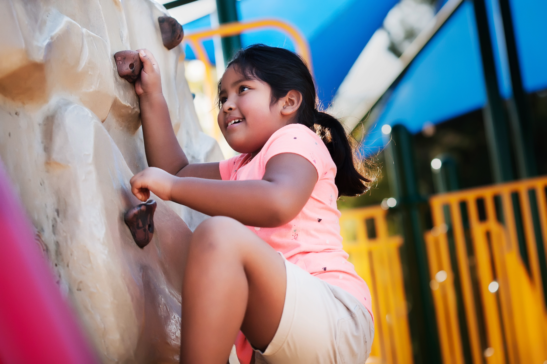 Young girl climbing on a rock climbing wall at a playground.