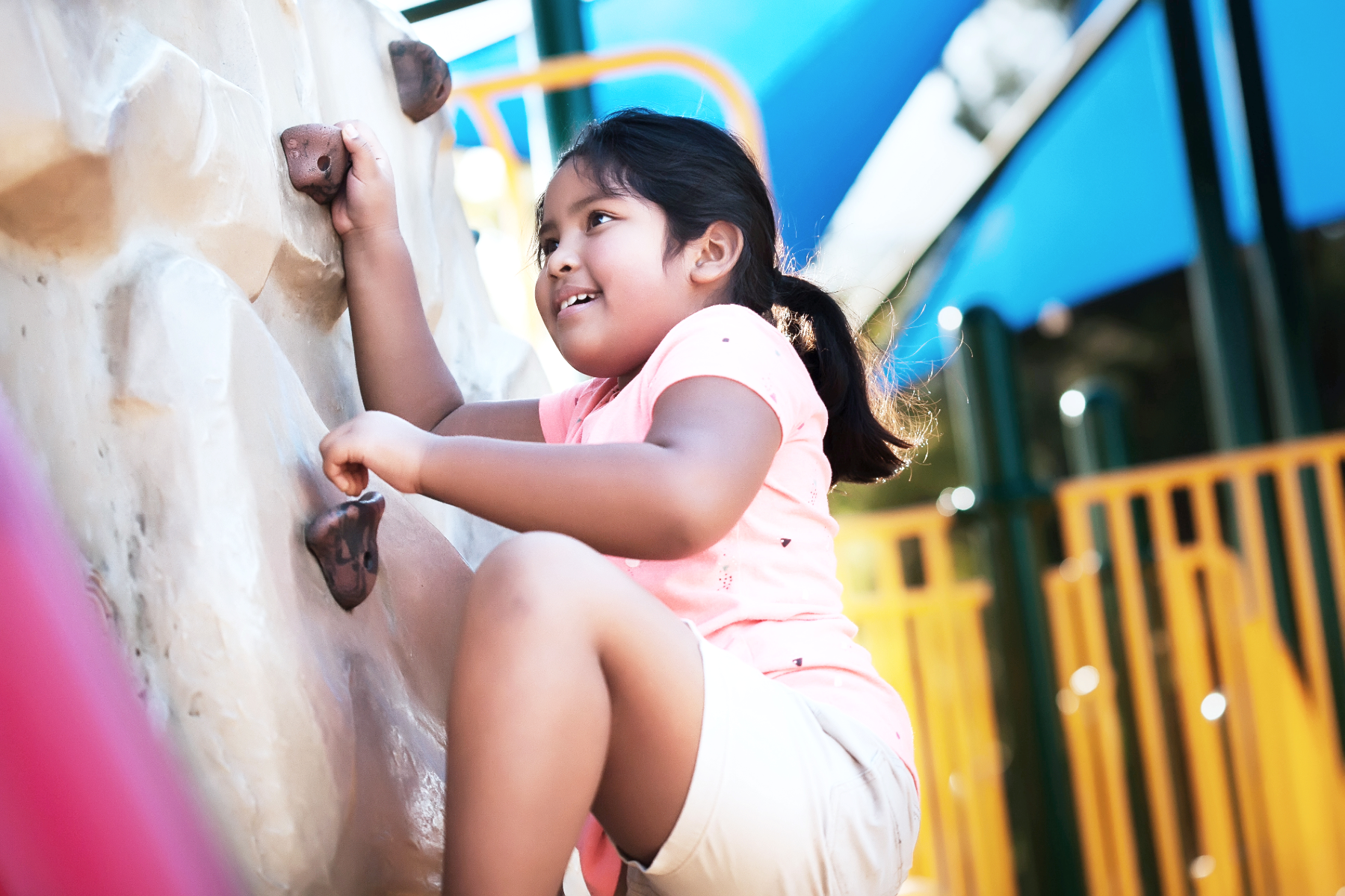 Young girl climbing on a rock climbing wall at a playground.