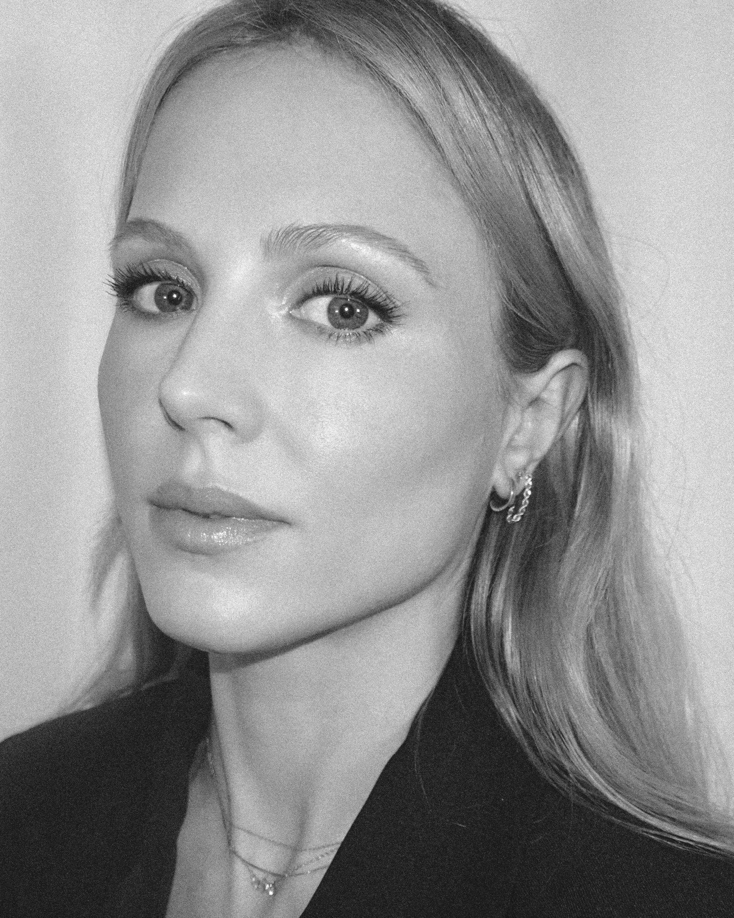 Black-and-white close-up portrait of a woman with light hair, wearing earrings and a necklace, looking slightly to the side. Makeup Artist Paris