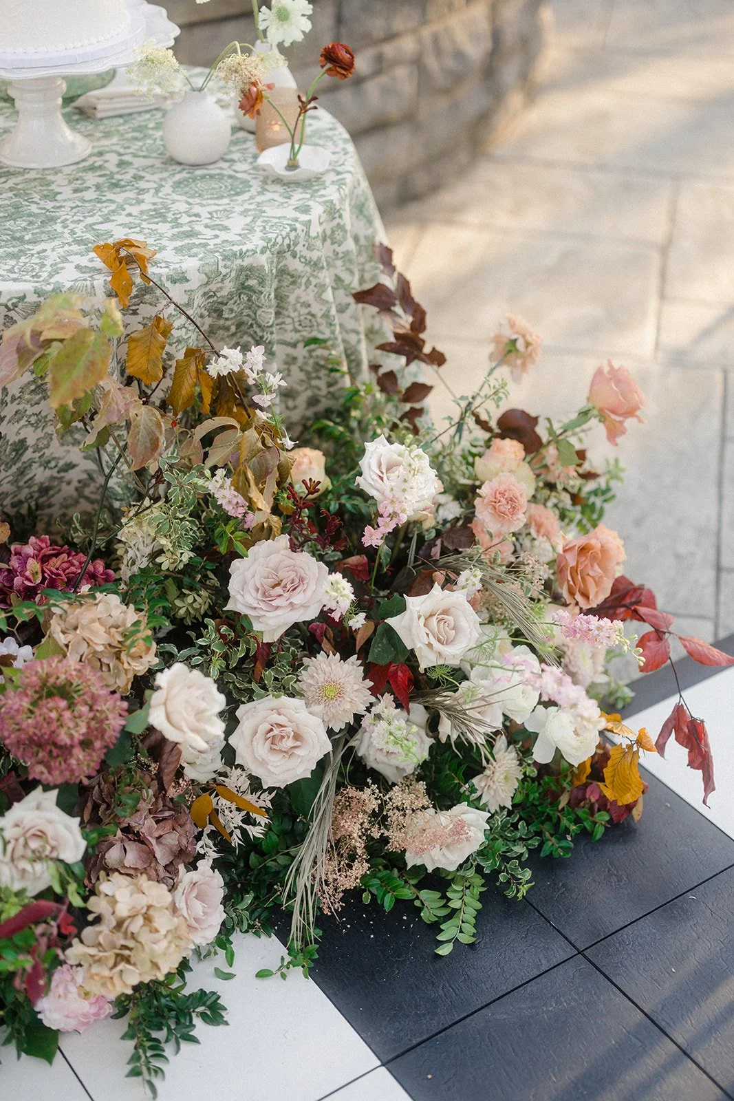 A floral arrangement with pink roses, white and pink dahlias, and greenery on a black and white table.