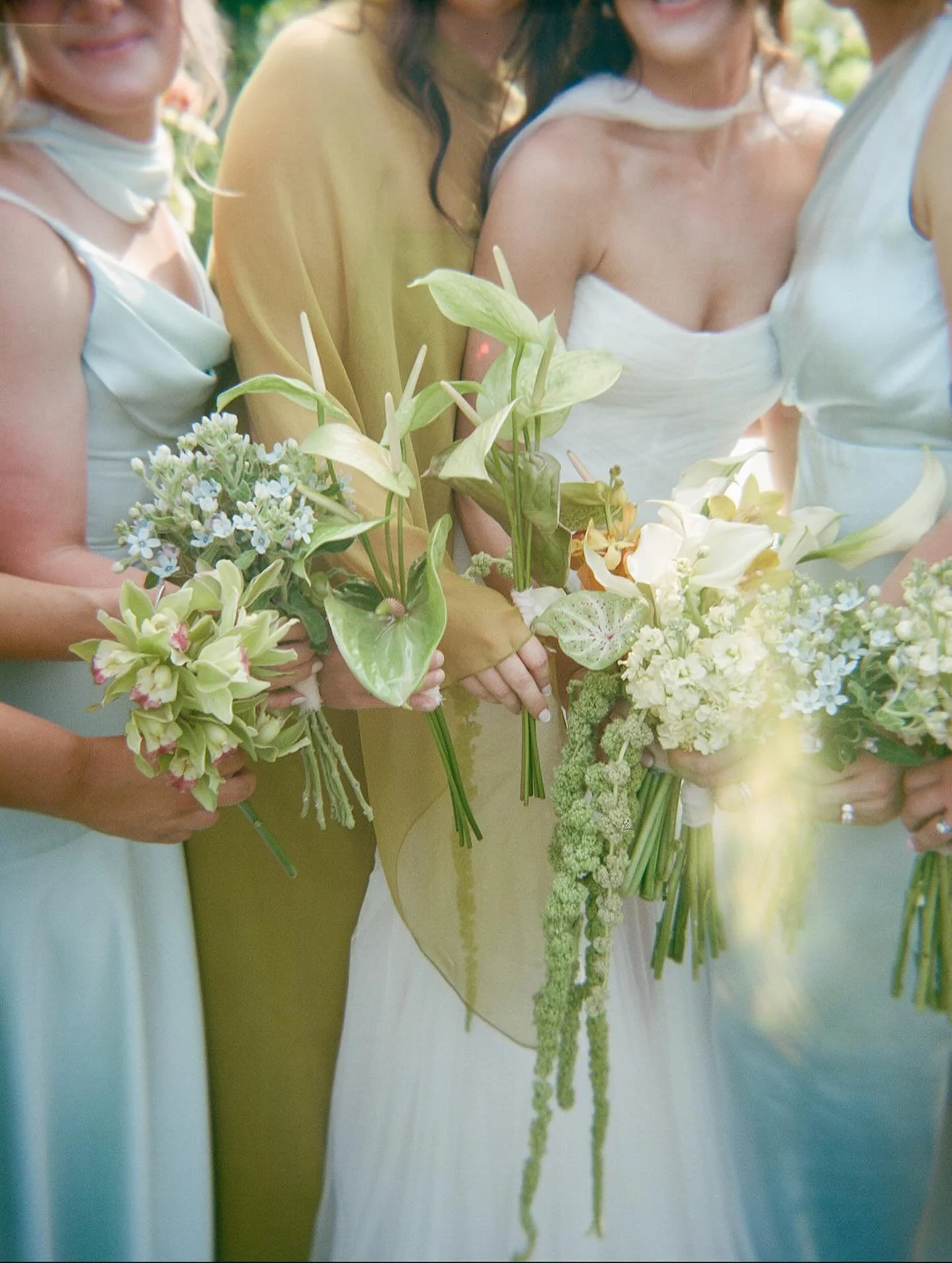 Close-up of wedding guests holding bouquets of white and green flowers at an outdoor wedding ceremony.