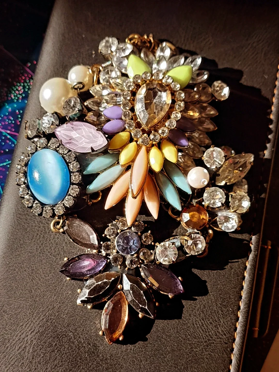 Colorful vintage-style brooch with various shapes and sizes of faux gemstones and pearls on black background.