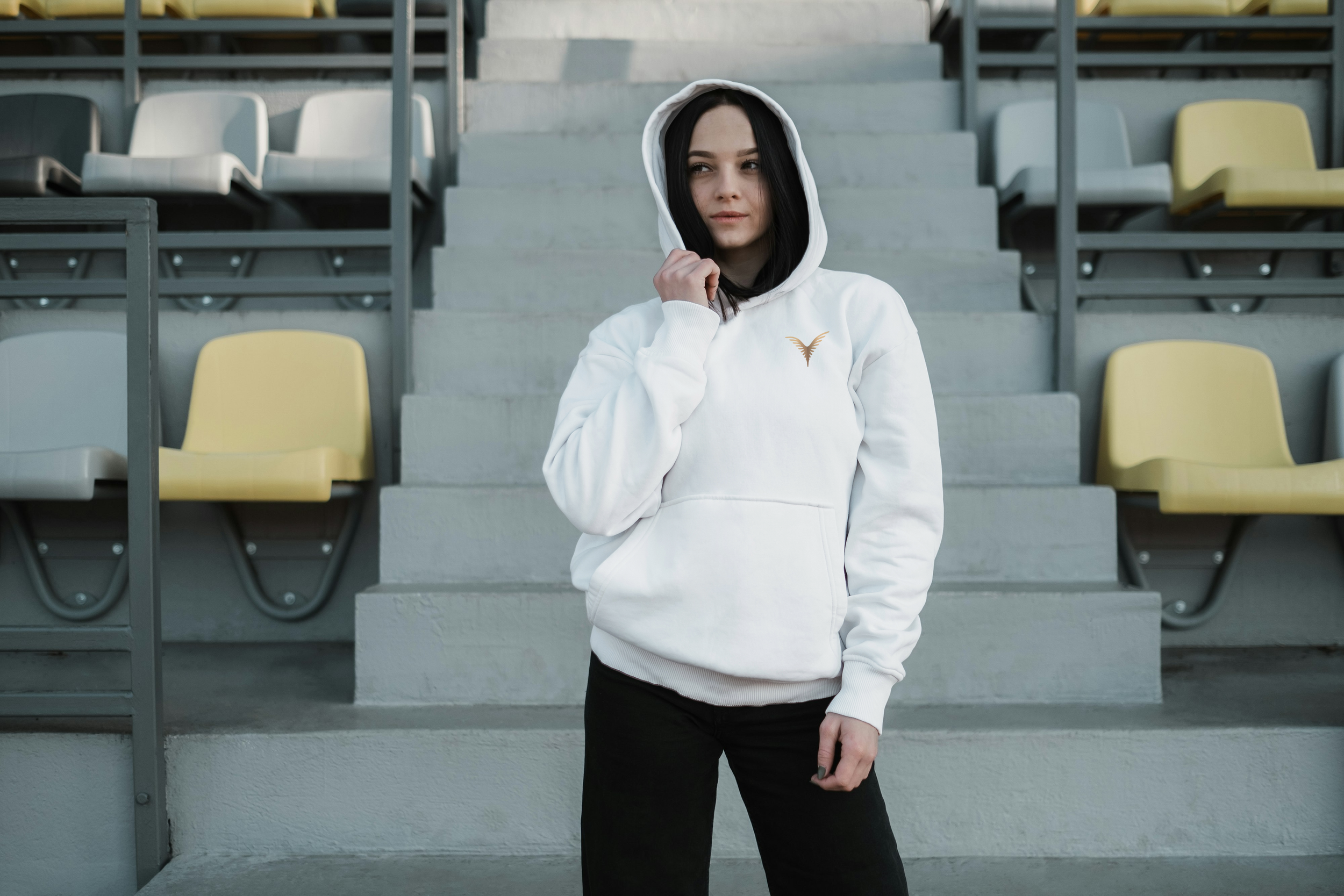 Jeune femme avec une capuche blanche et un sweat à capuche, debout dans une tribune sportive.
