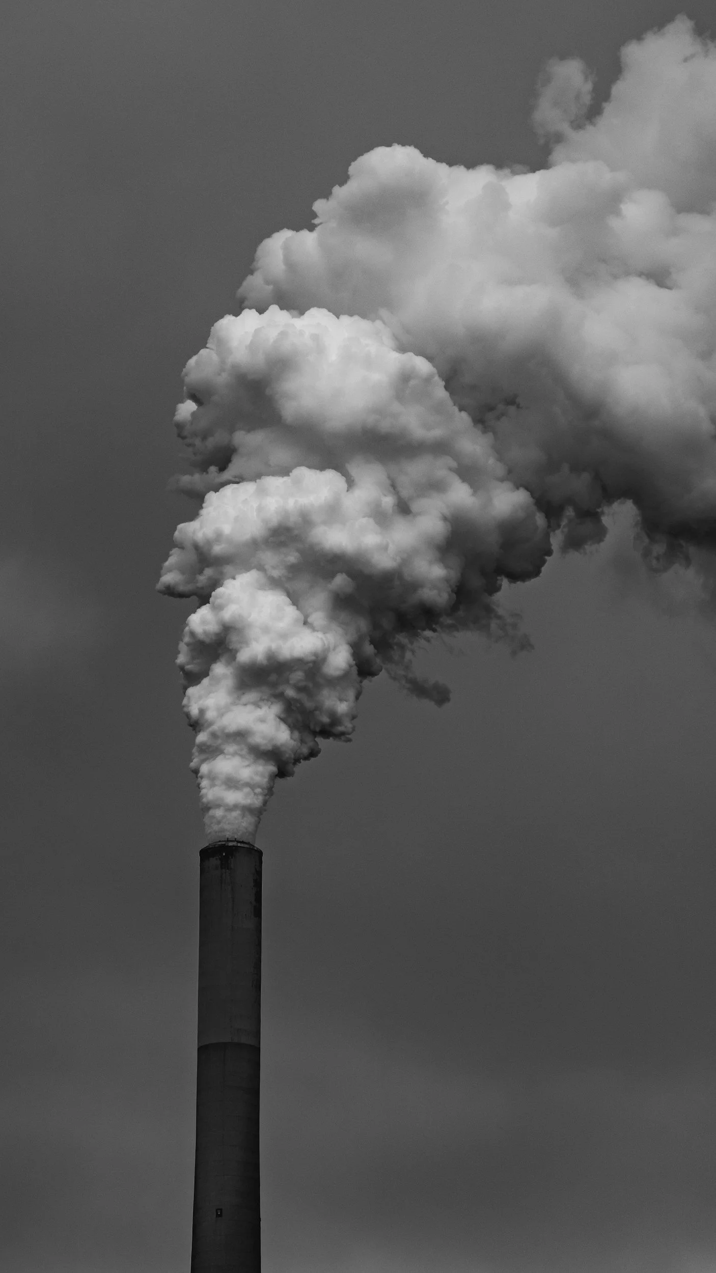 Black and white photo of a smokestack releasing thick smoke into the sky.
