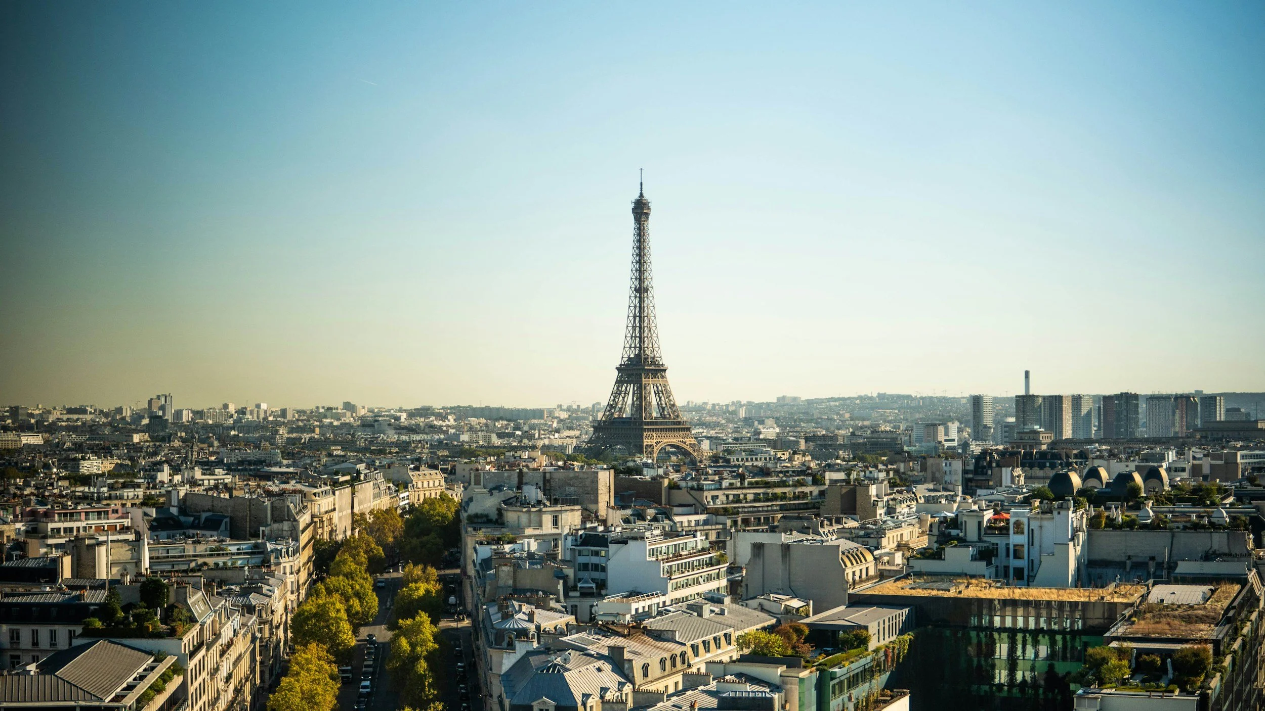 Paris cityscape with Eiffel Tower under clear sky, view of surrounding buildings and greenery.