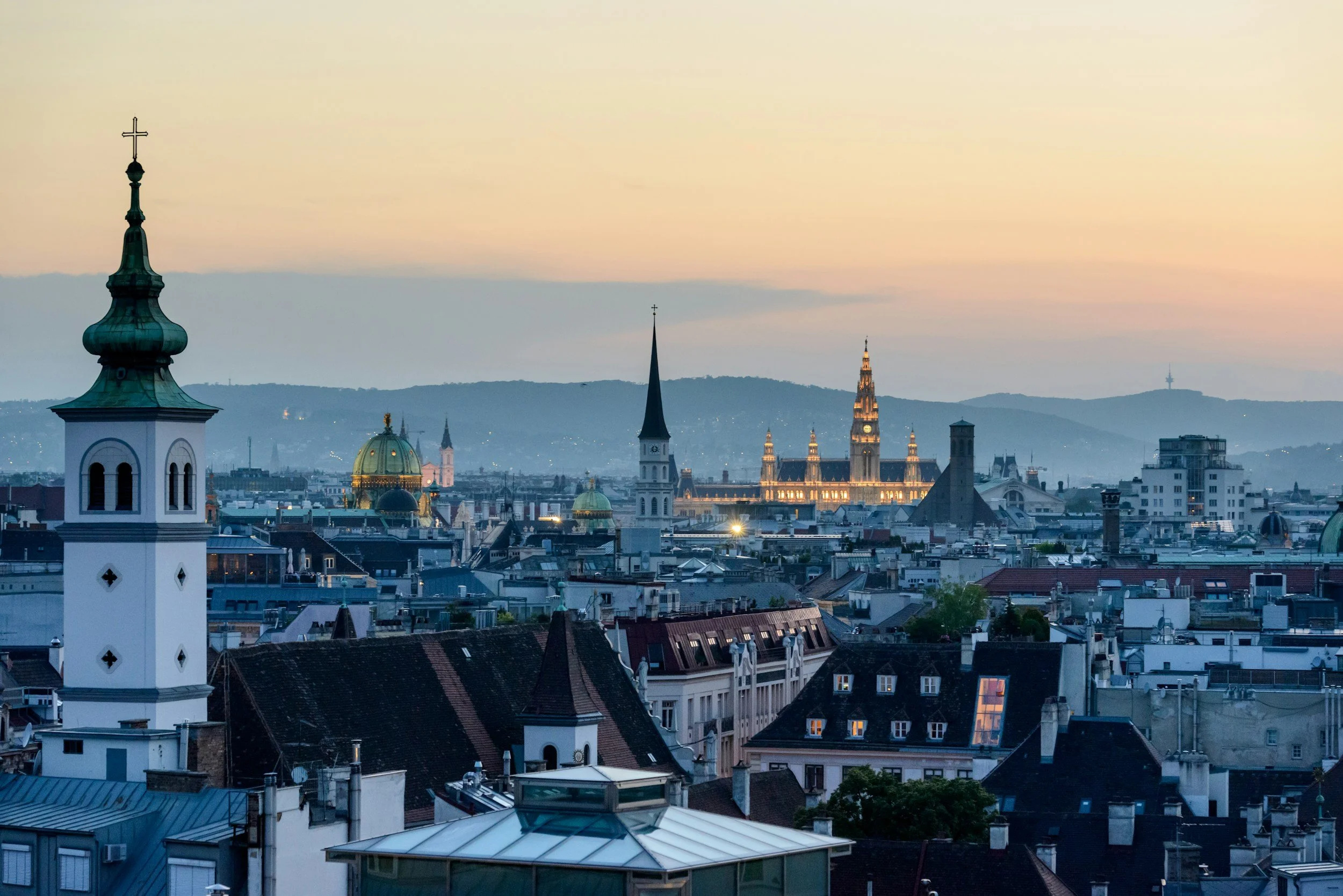 Cityscape of Prague at sunset with iconic spires and domes, including the Prague Castle and Charles Bridge.