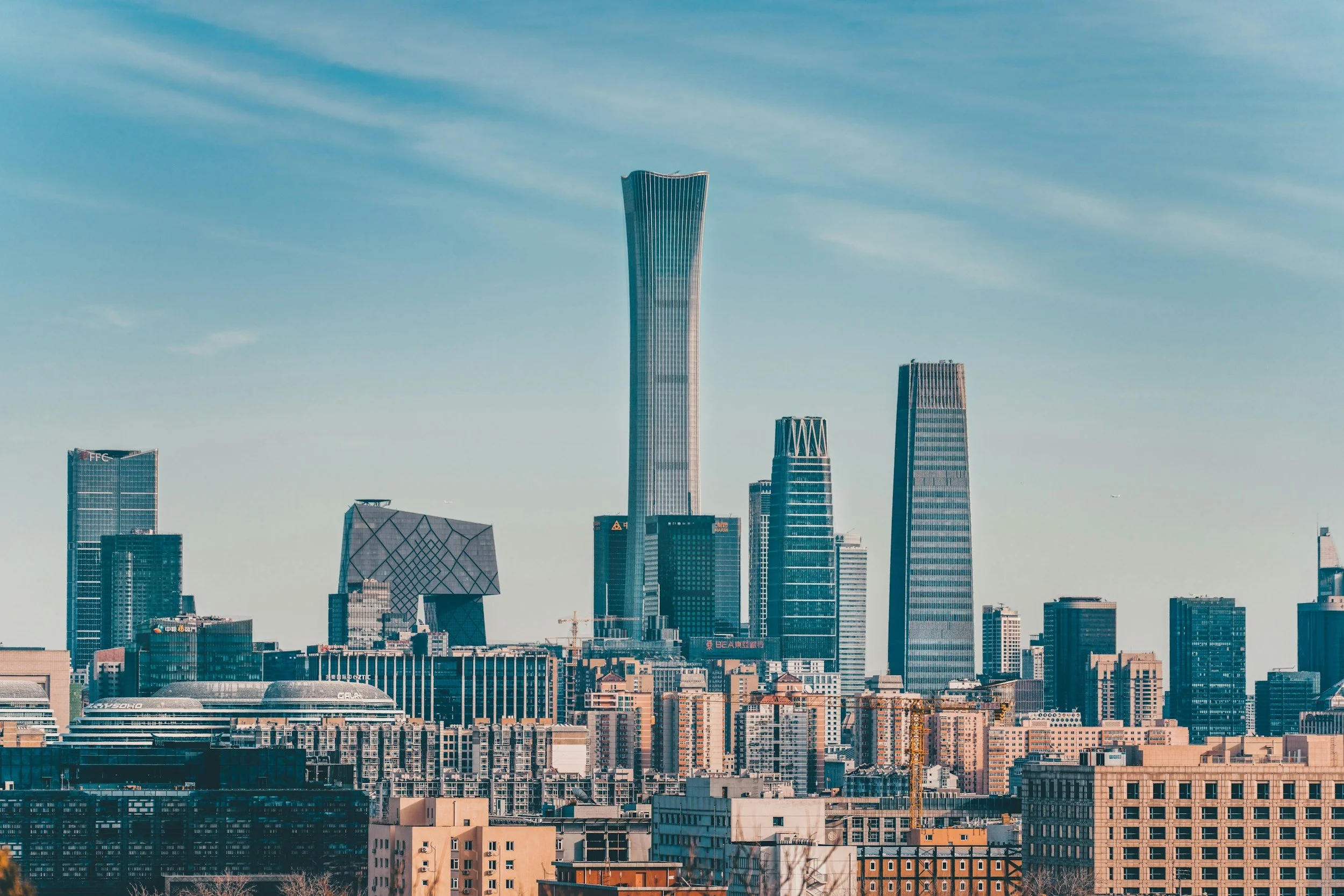 City skyline with modern skyscrapers, including one tall, uniquely shaped building, under a partly cloudy sky.