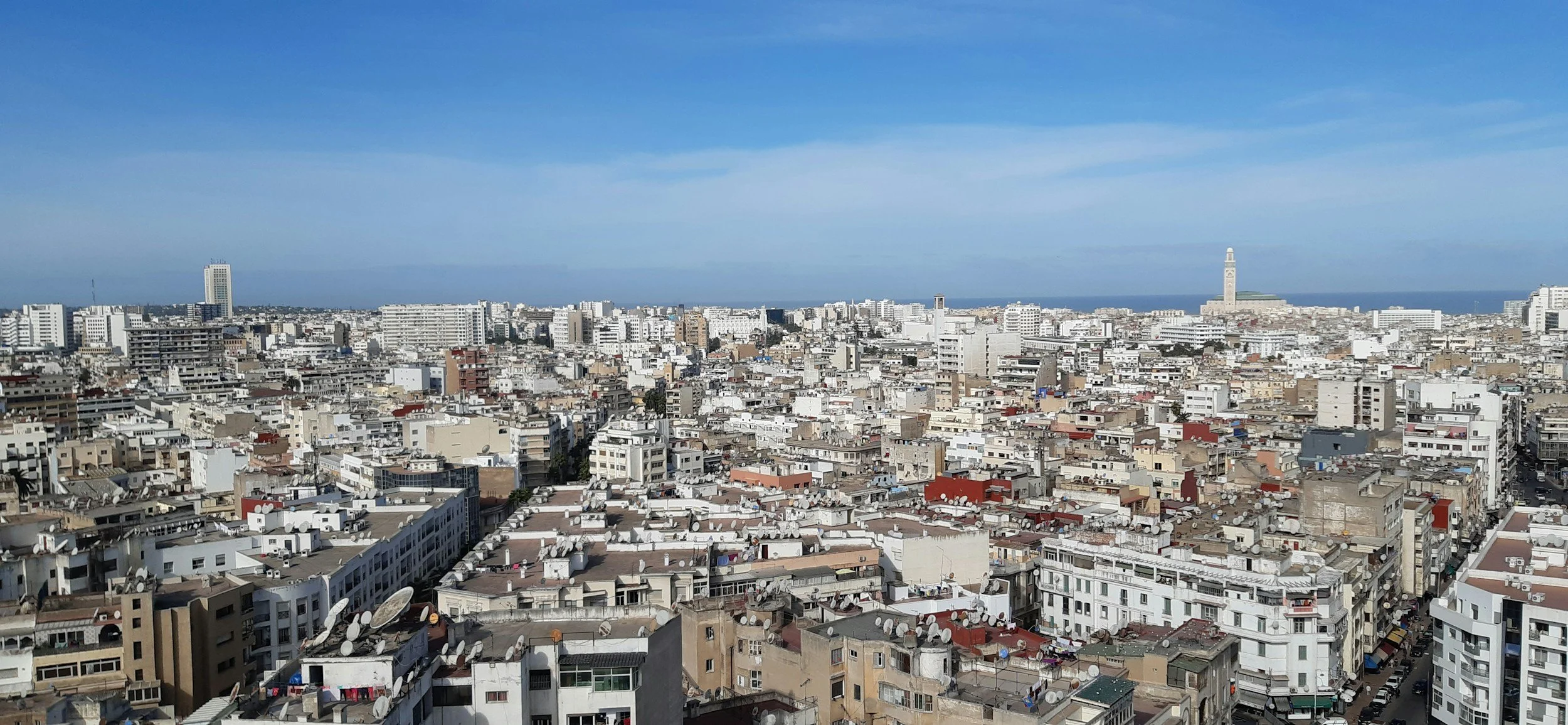 Cityscape of densely packed buildings and rooftops in a coastal city under a clear blue sky.