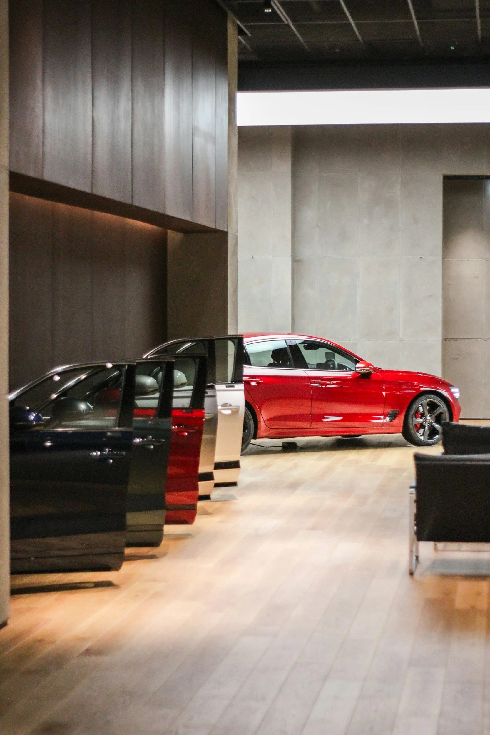 Red sports car parked inside a modern showroom with minimalist design. The background features plain concrete walls and a horizontal light fixture.