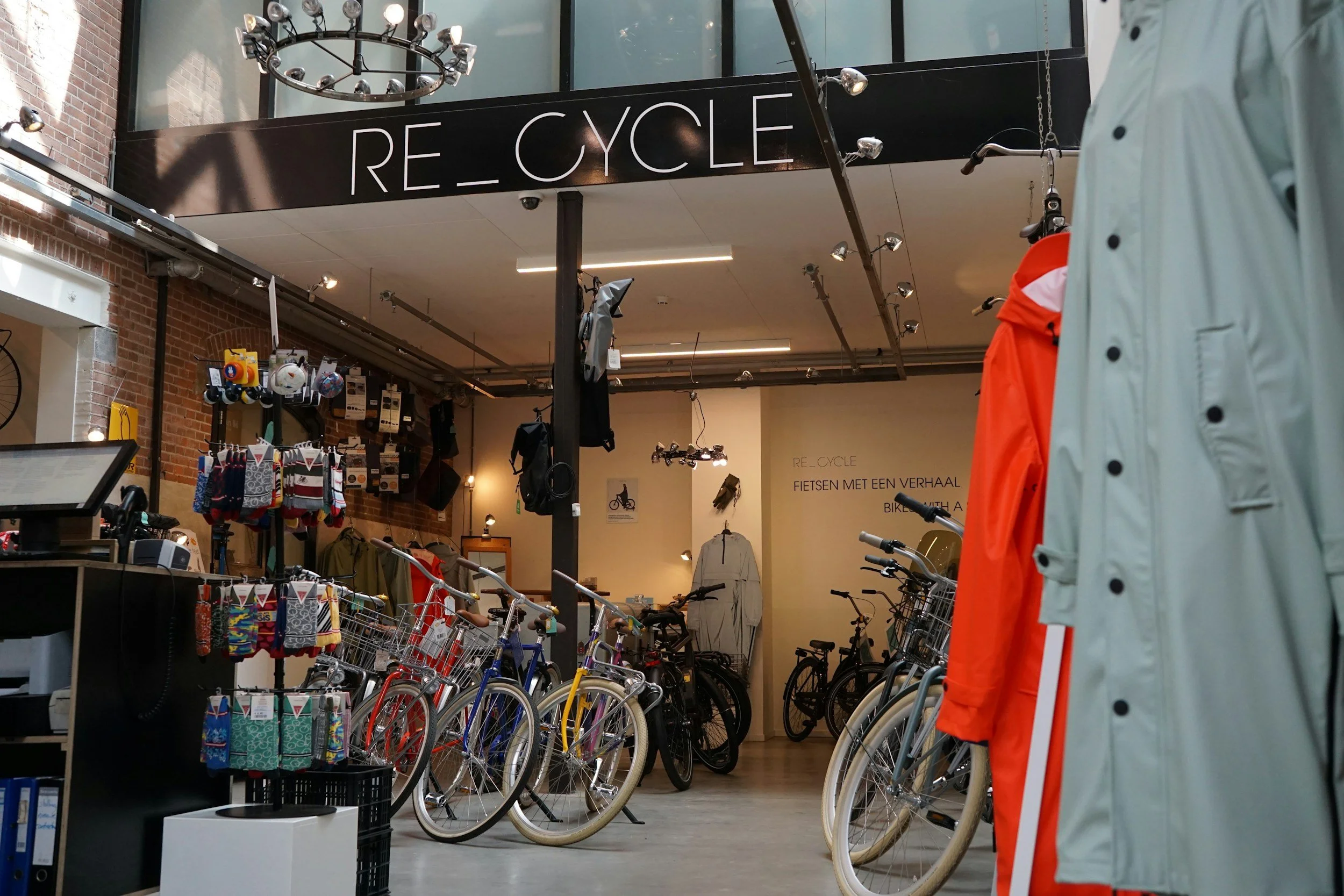 Inside a bicycle shop with bicycles displayed for sale, clothing items like jackets and socks, and a sign that reads "RE_CYCLE".