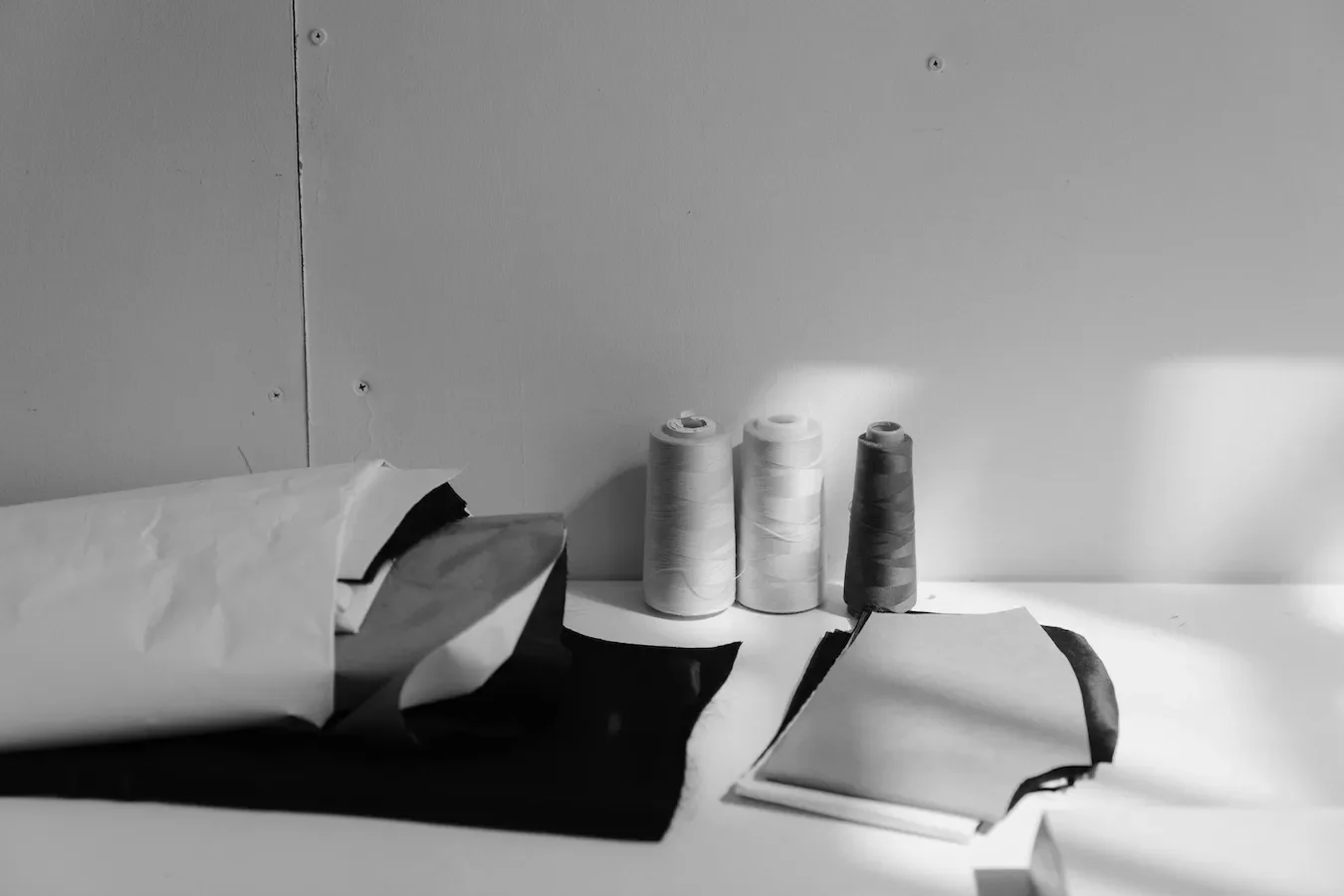 Spools of thread, a partially opened package, and a closed notebook arranged on a surface in front of a plain wall.