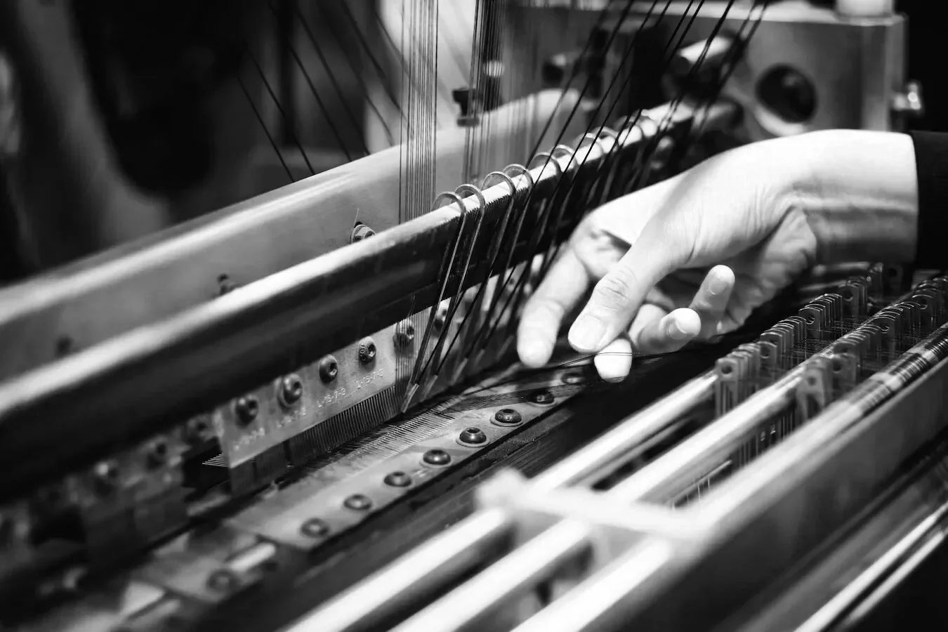 A person's hand adjusting strings inside a piano.