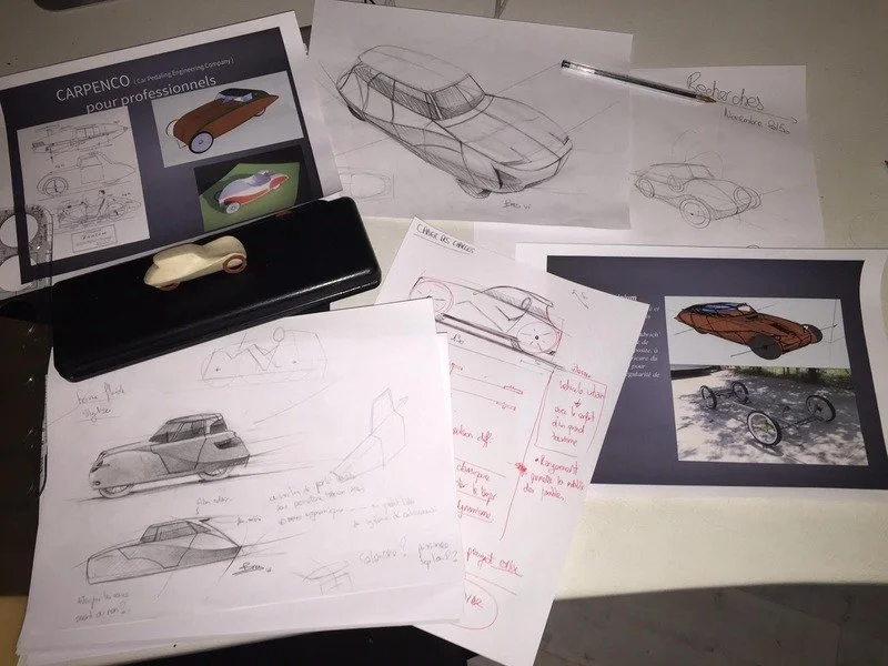 The very beggining of ELYSEE by Yxelon collection of sketches and printed images of cars, along with a black case, a computer mouse, and a pen on a white desk.