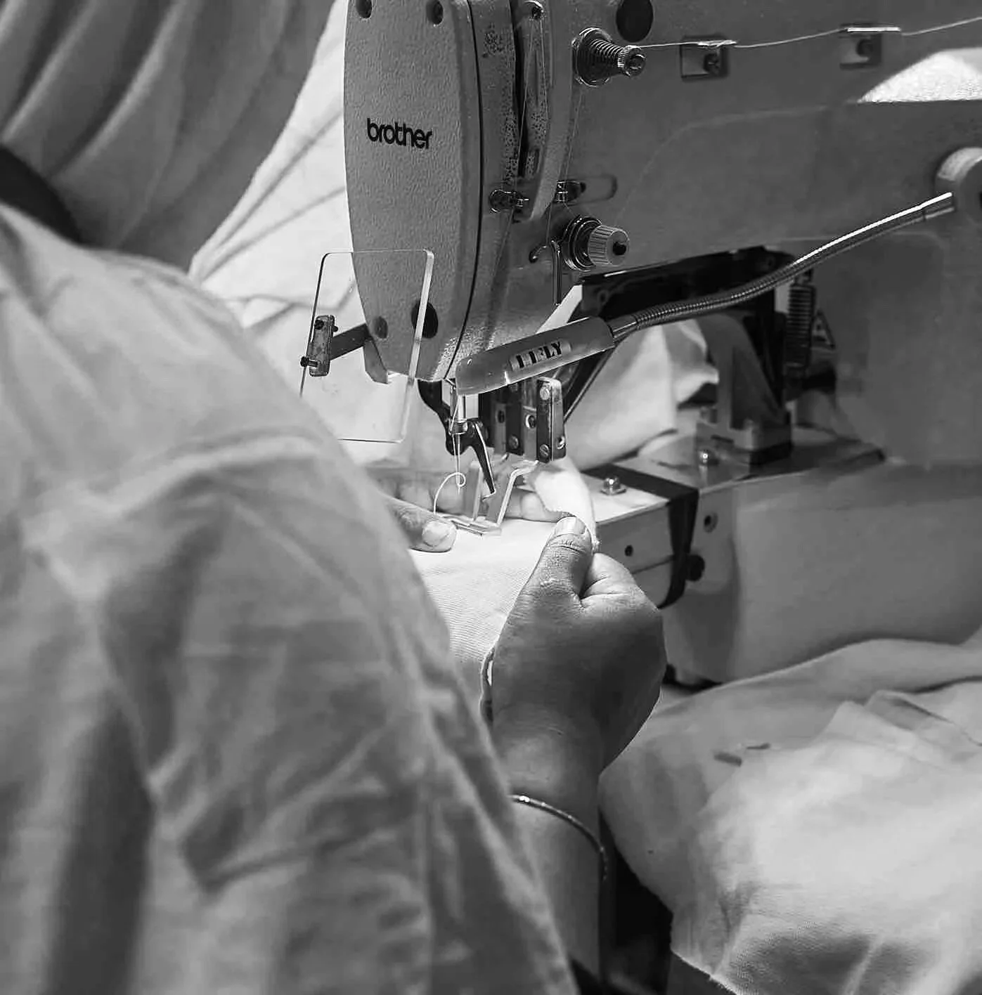 Black and white photo of a person sewing fabric with a sewing machine, wearing gloves.