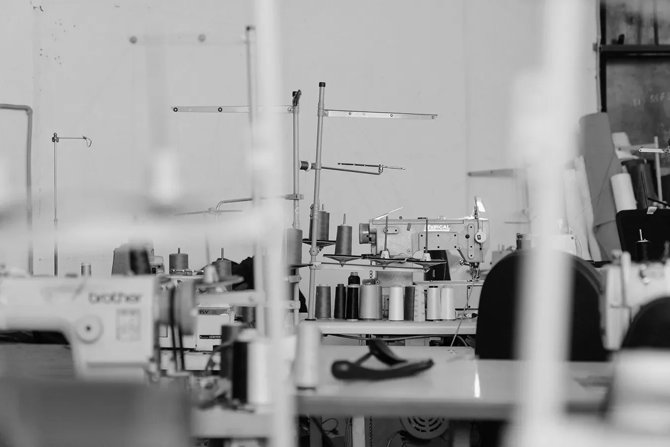 Black and white image of a sewing workshop with various sewing machines, spools of thread, and fabric materials.