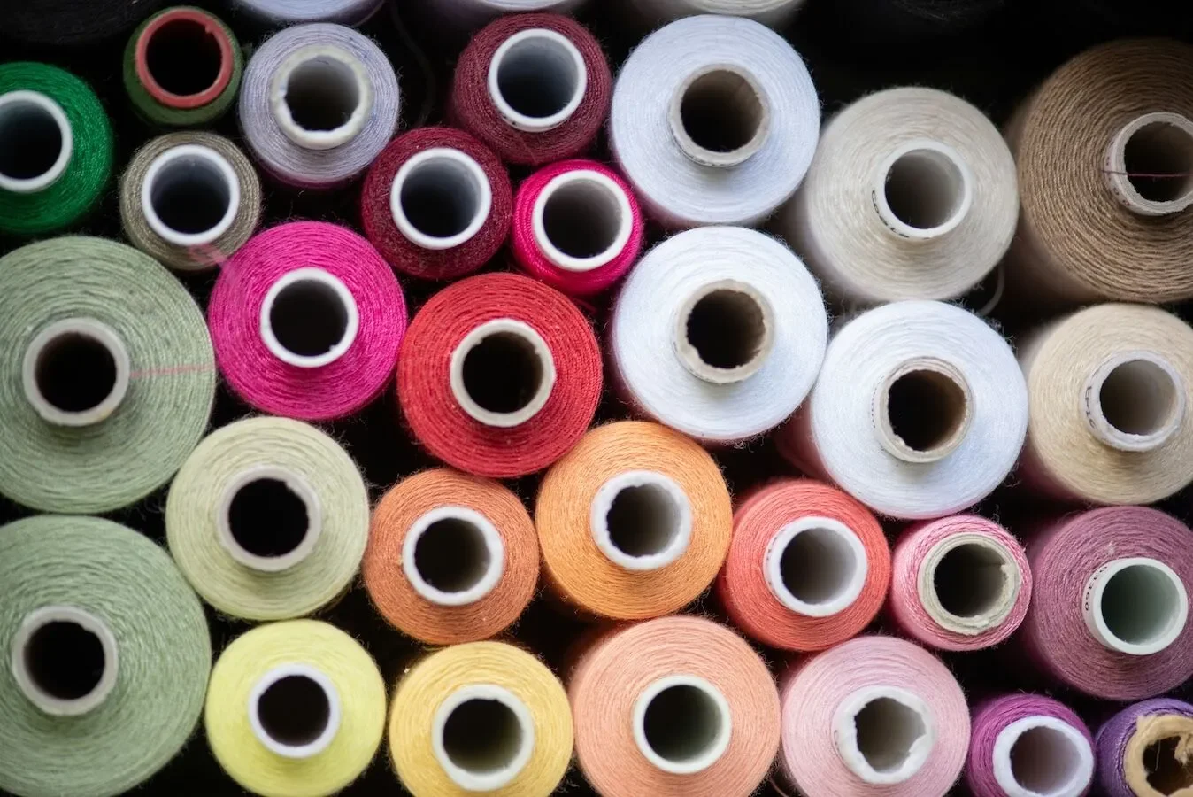 Multiple spools of colorful sewing thread arranged closely together, with various shades including pink, white, green, yellow, orange, and purple.