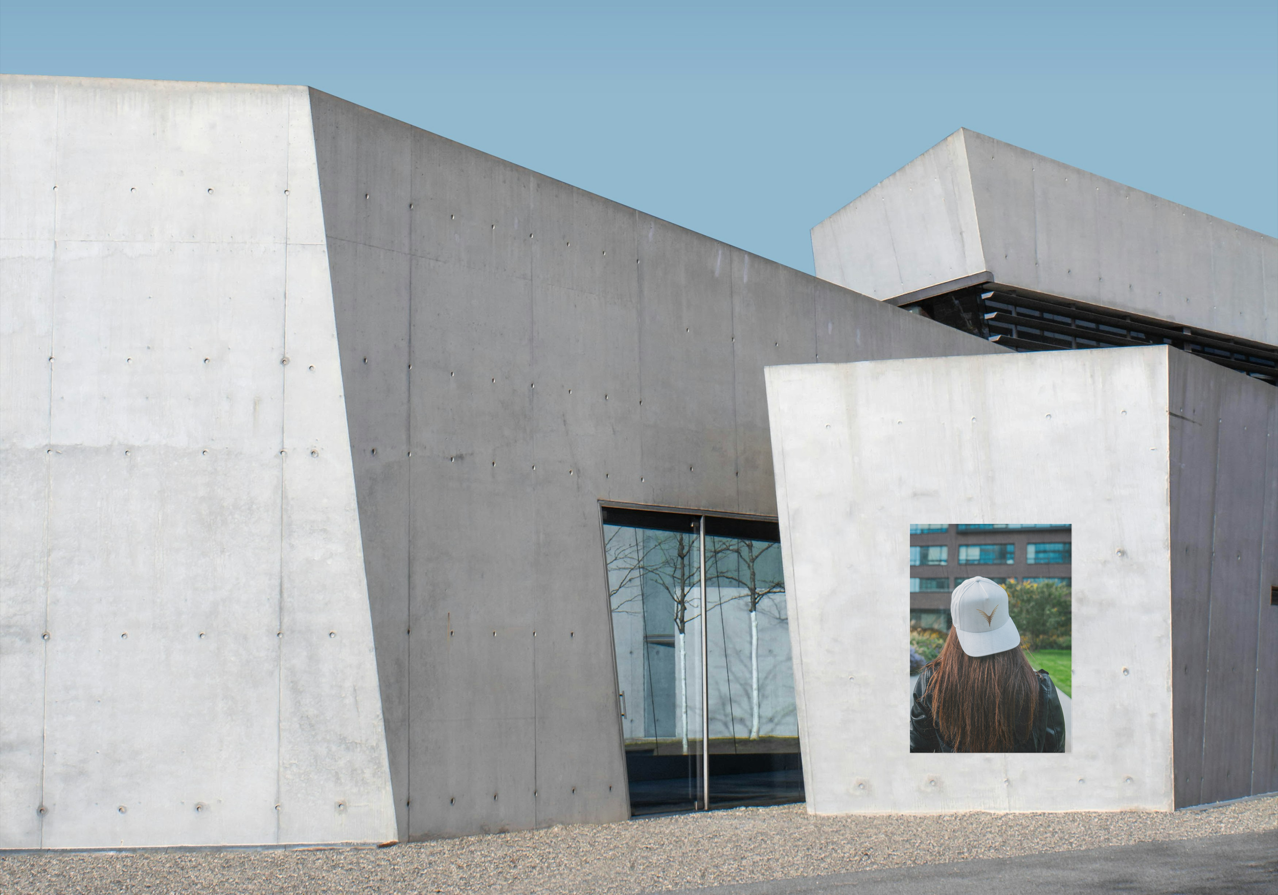 Une structure architecturale moderne en béton avec des formes géométriques angulaires. Une femme portant une casquette blanche regarde à travers un cadre ouvert dans le mur, avec des arbres et un bâtiment en arrière-plan.