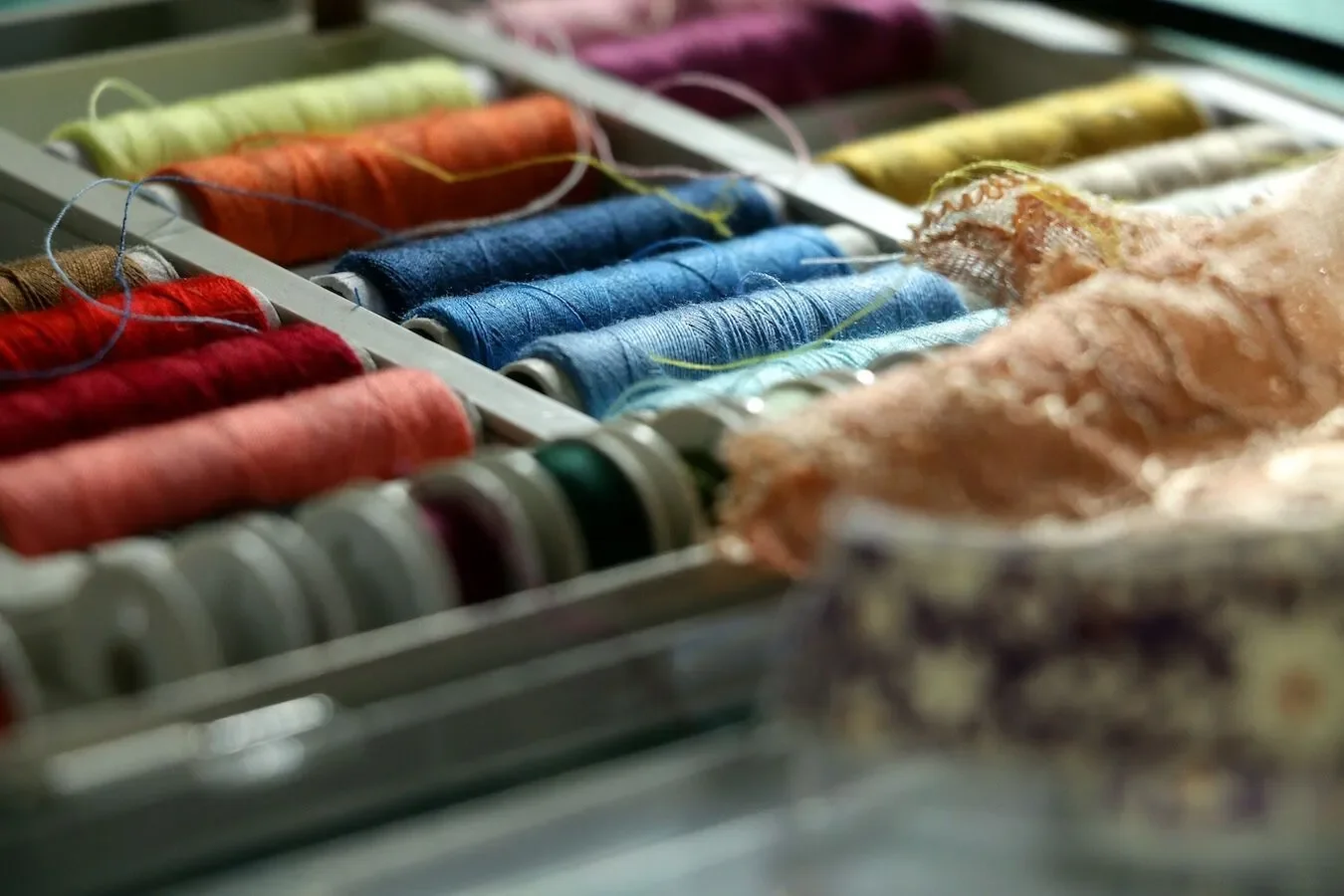 Close-up of colorful embroidery threads organized in a box, with some partially used spools and some fabric pieces in the foreground.