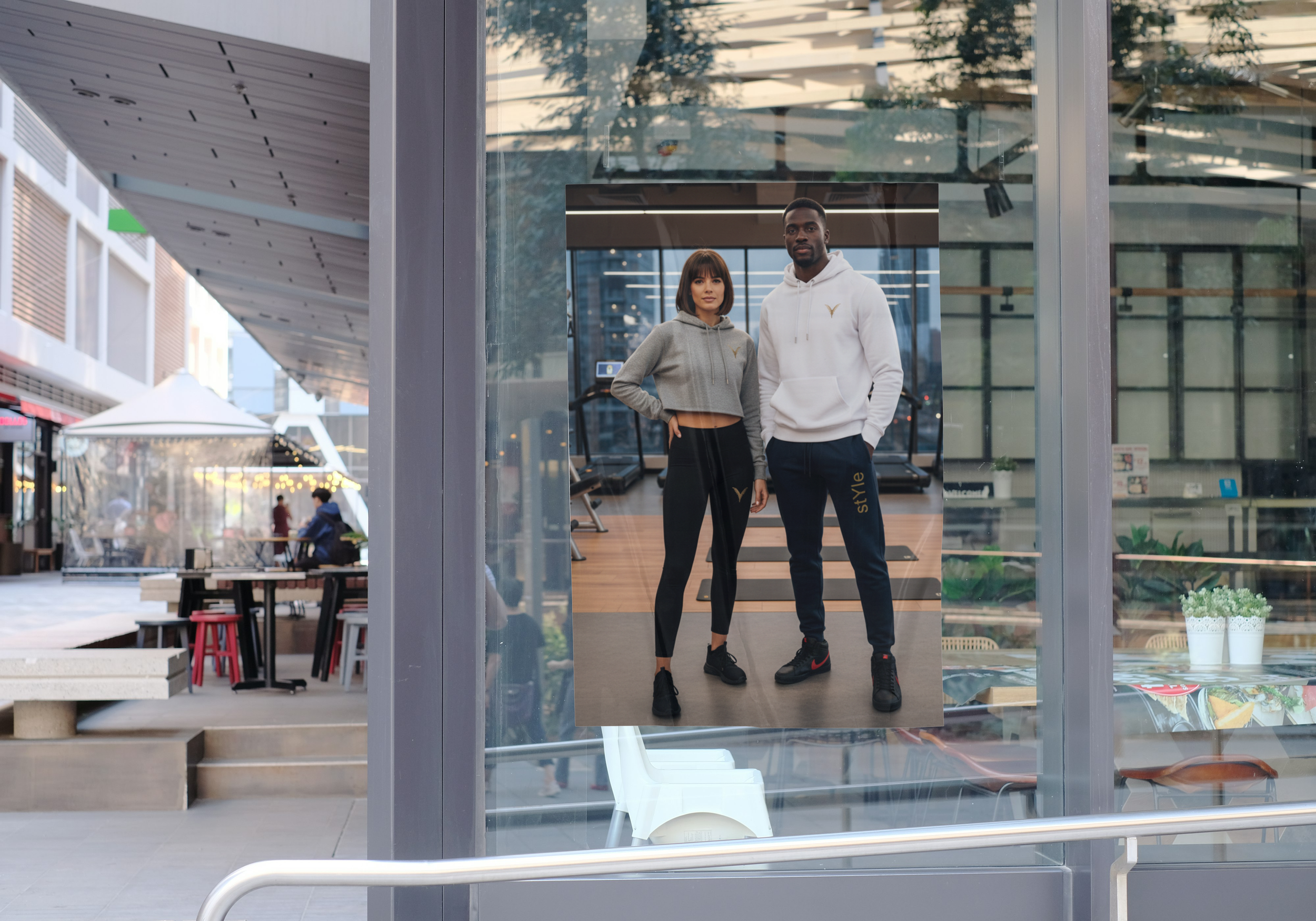 Photo d'une affiche de deux personnes en tenue de sport à l'intérieur d'une salle de sport, vue à travers une vitrine dans un environnement urbain.