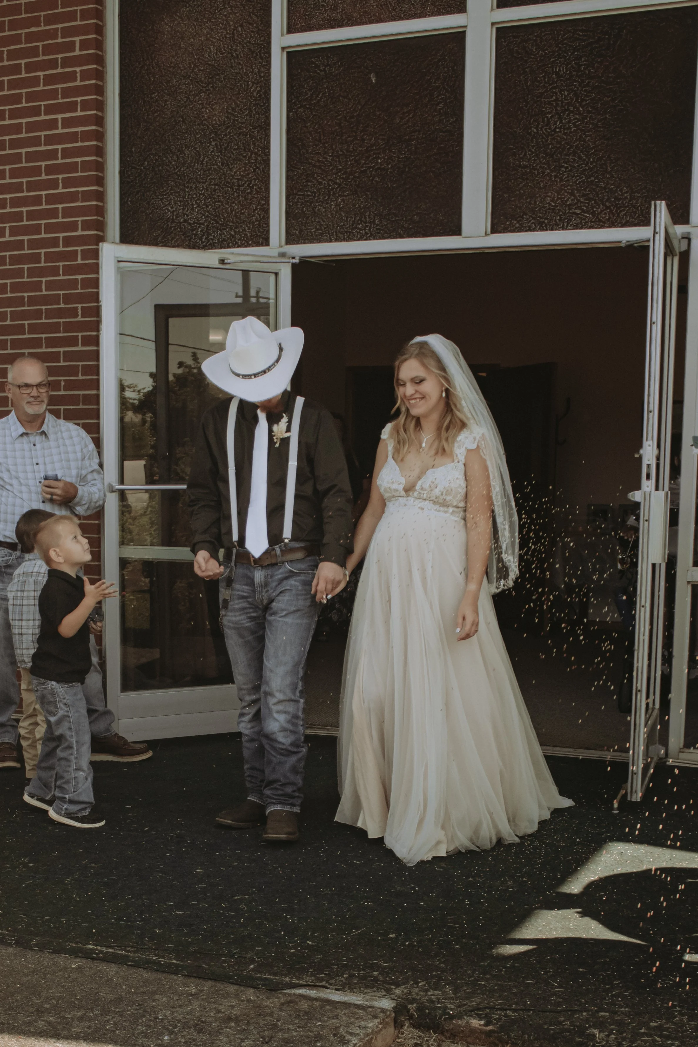 Bride and groom leaving a wedding venue through a door, holding hands, with guests celebrating nearby.