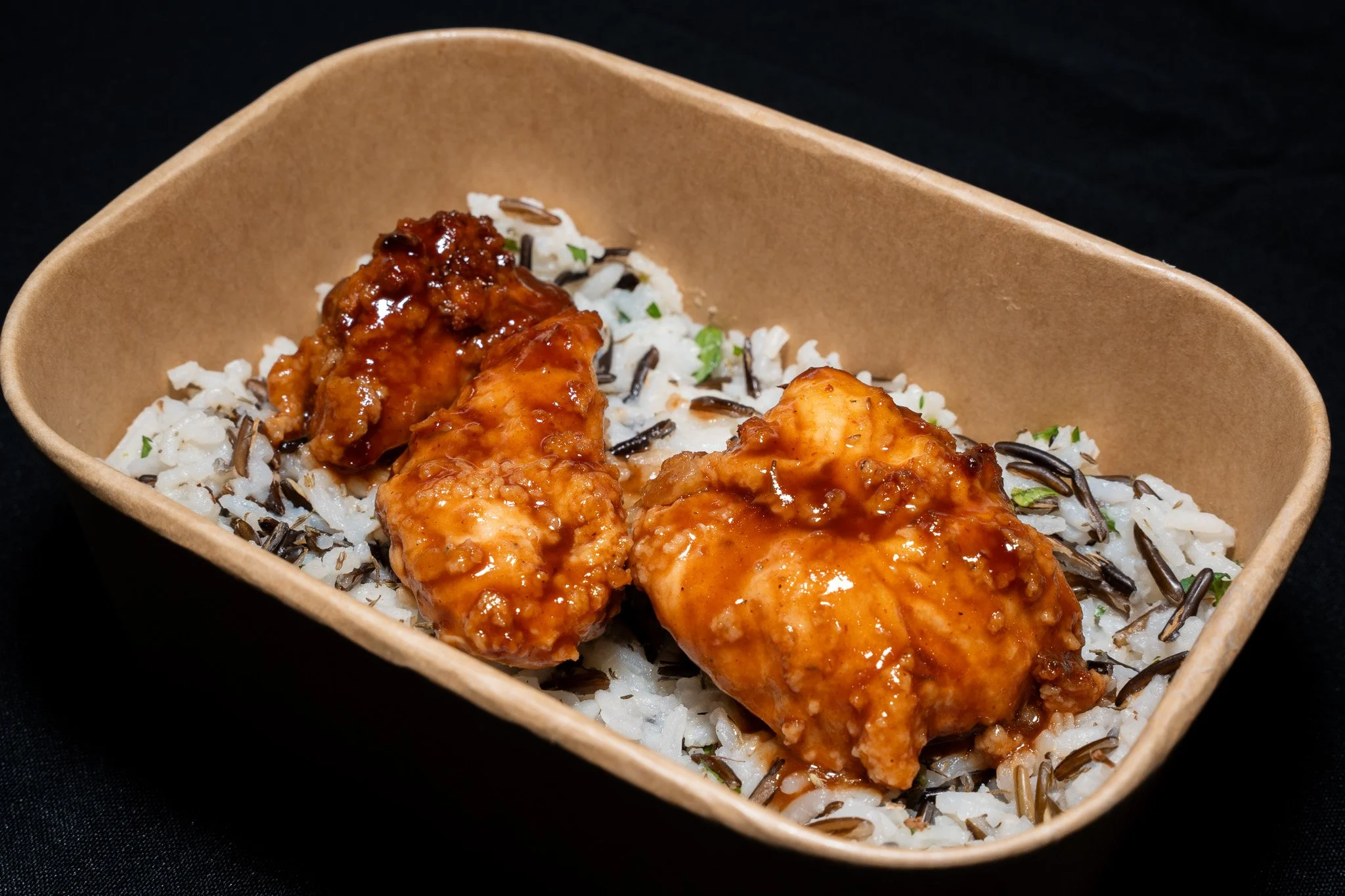 A bowl of rice topped with two pieces of glazed chicken in sauce.