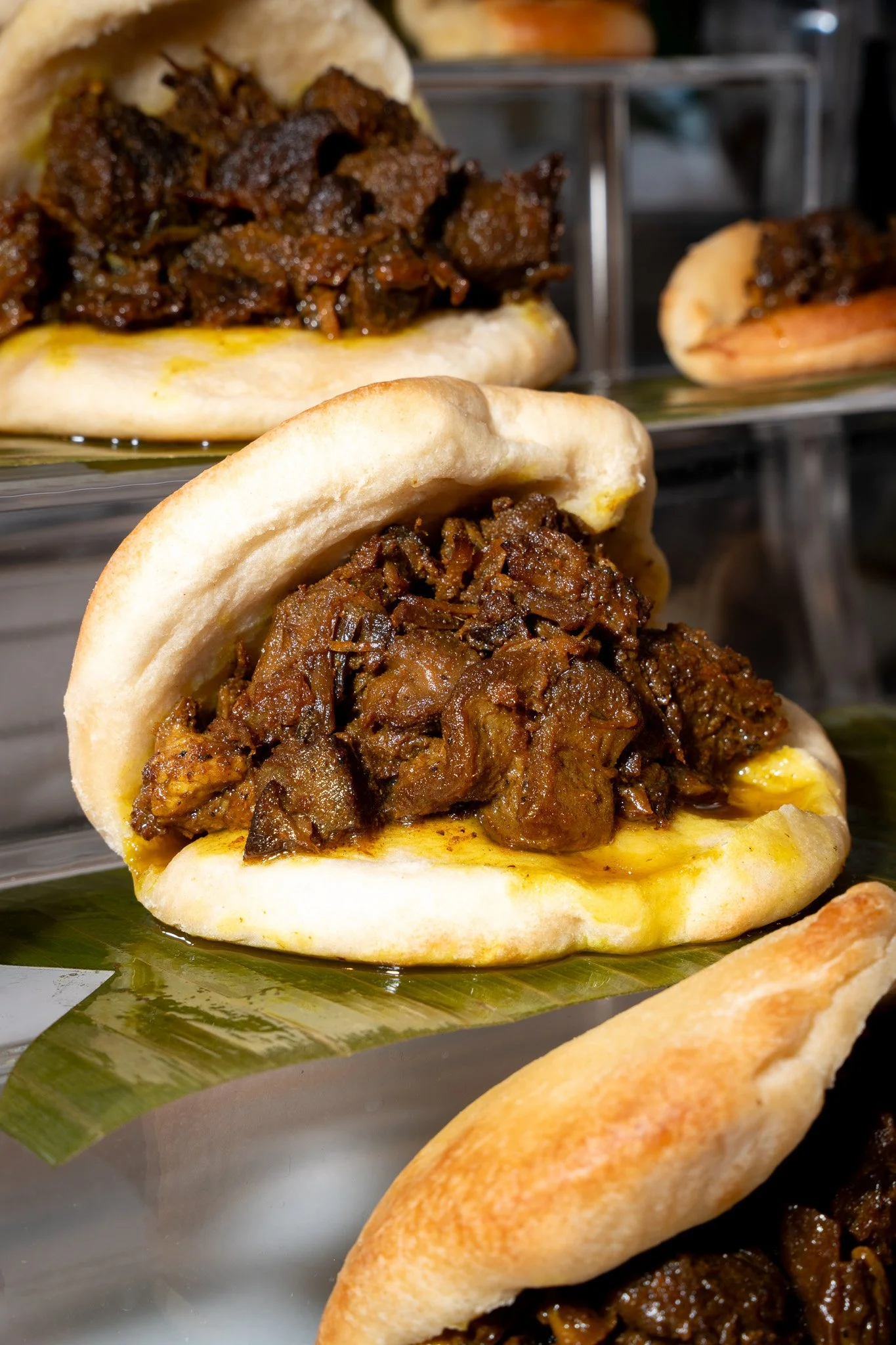 Close-up of beef sandwiches with soft buns and caramelized onions on a reflective surface.