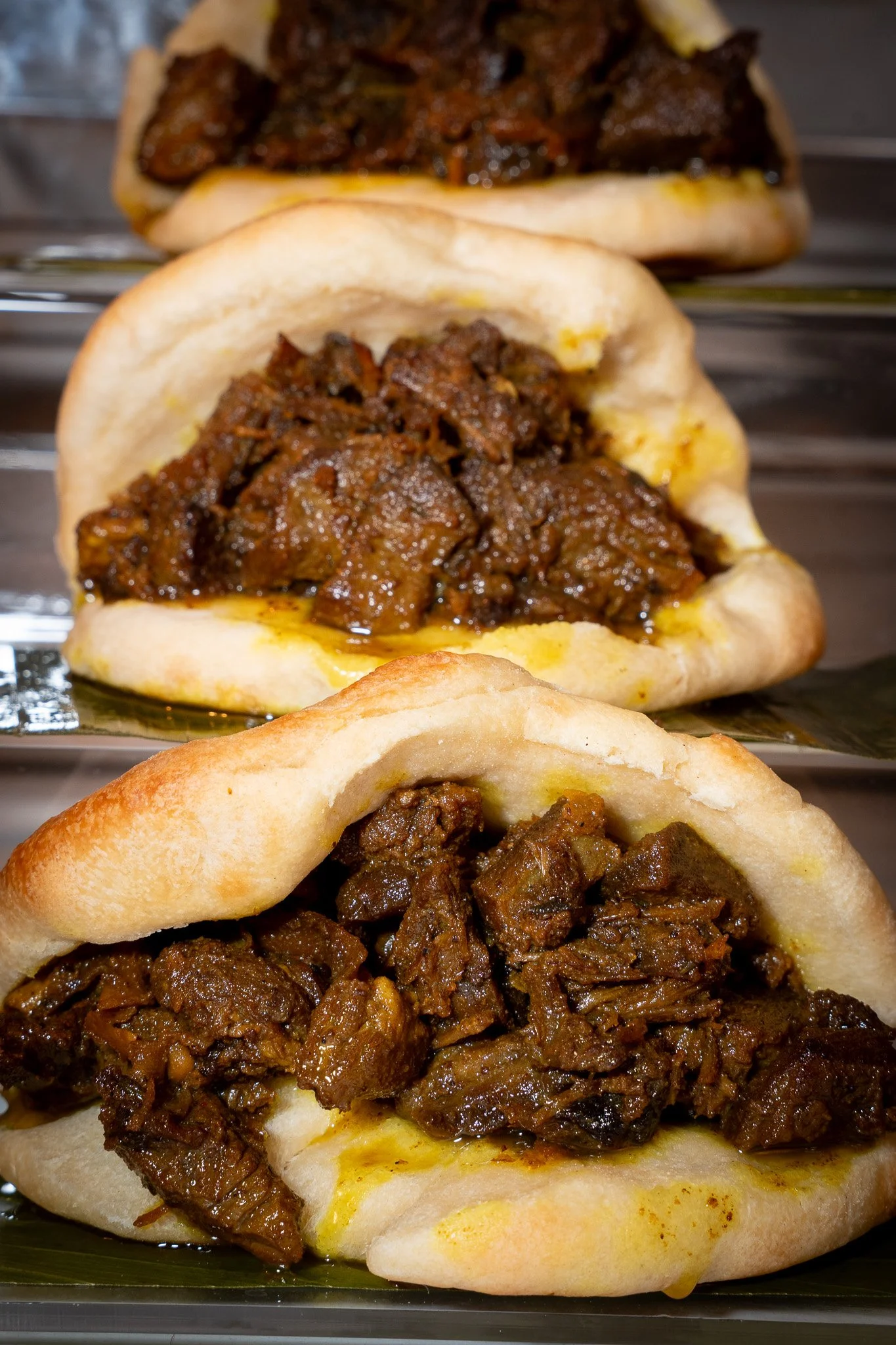 Close-up of three beef barbecue sandwiches with shredded beef in buns.