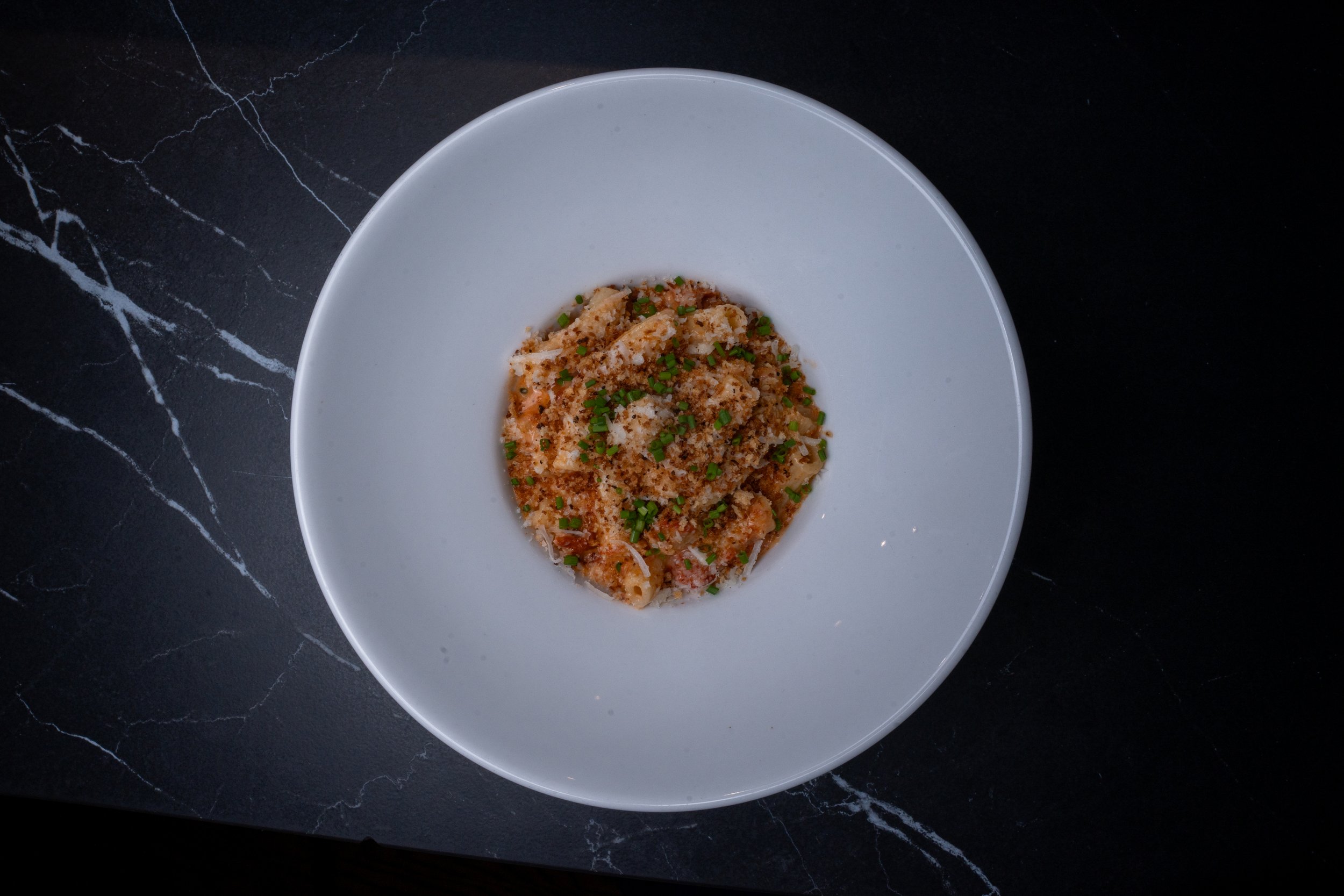 A white bowl of pasta topped with chopped chives on a black marble surface.