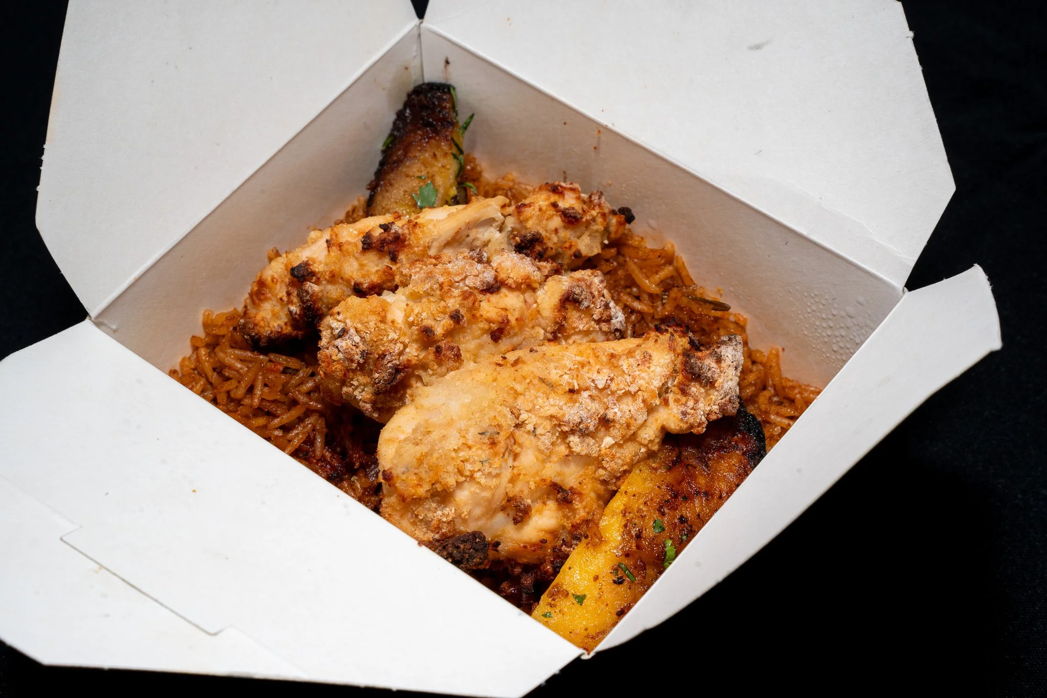 Takeout box containing fried chicken, seasoned rice, roasted zucchini, and roasted yellow squash.