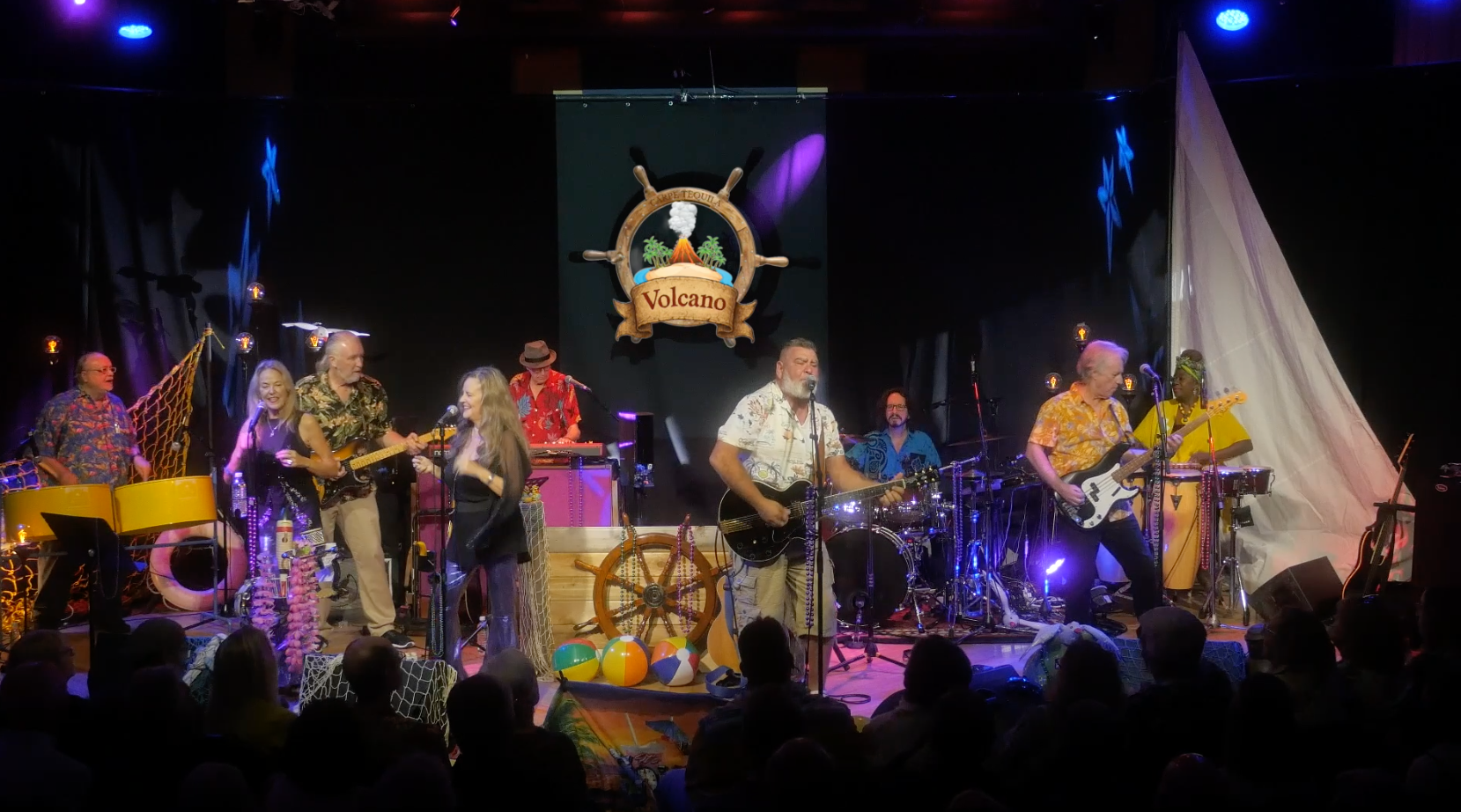 9 members of the Volcano Band performing music on a black stage with the audience in front
