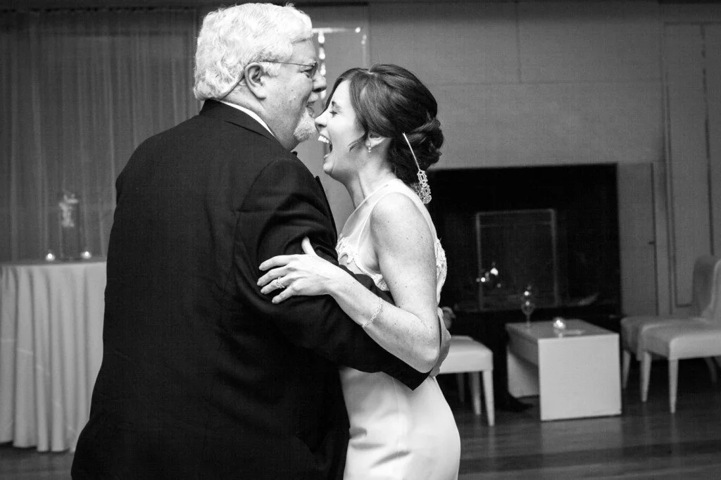 A couple, an older man and a younger woman, dancing closely and smiling at each other in an indoor setting.
