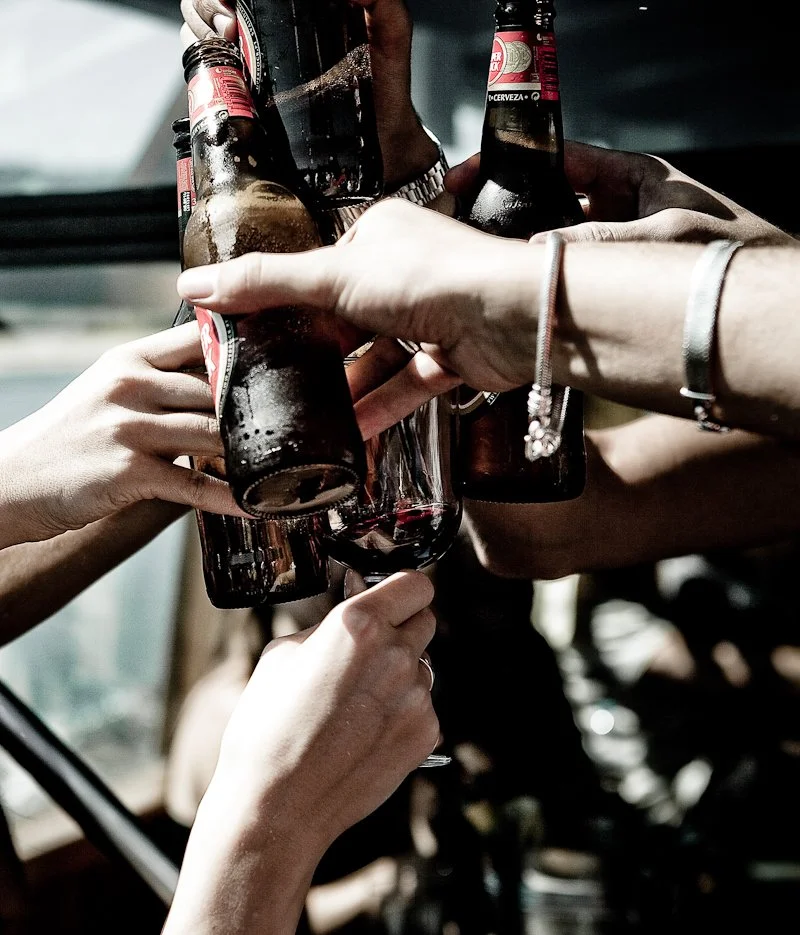Group of people raising their bottled drinks in a toast, celebrating together.