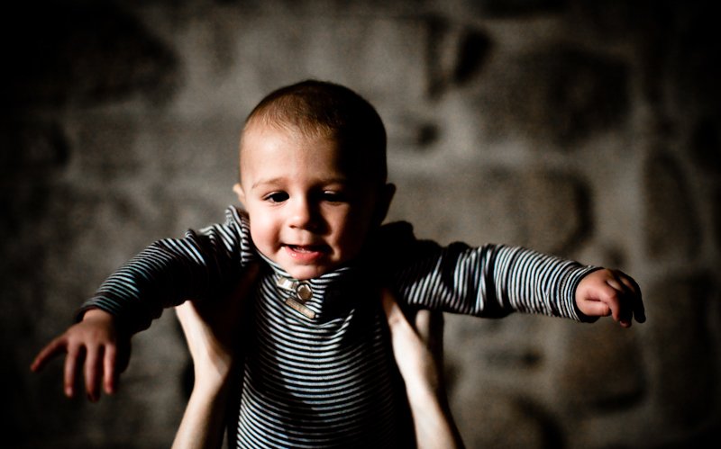 Child being held up by two hands, smiling against a dark, textured background.