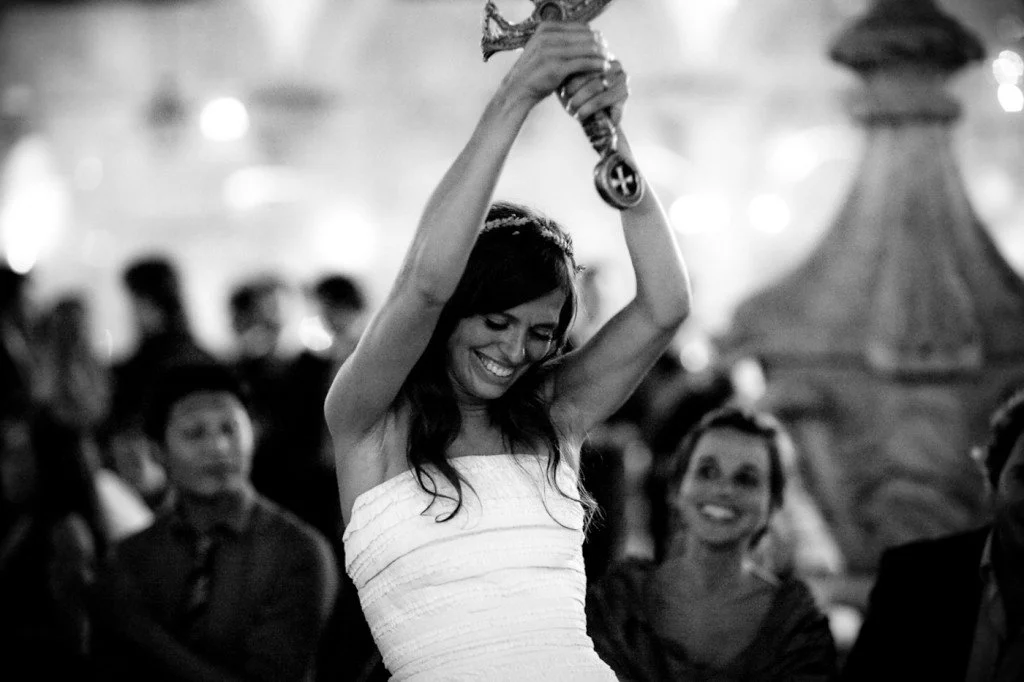 A woman in a strapless dress holding a trophy above her head, smiling with her eyes closed, in a crowded indoor setting.