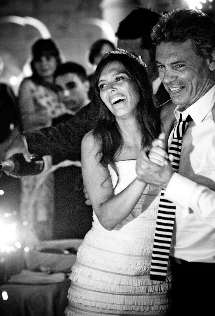 A woman and a man are dancing together at a celebration with other people in the background, in a black and white photo.