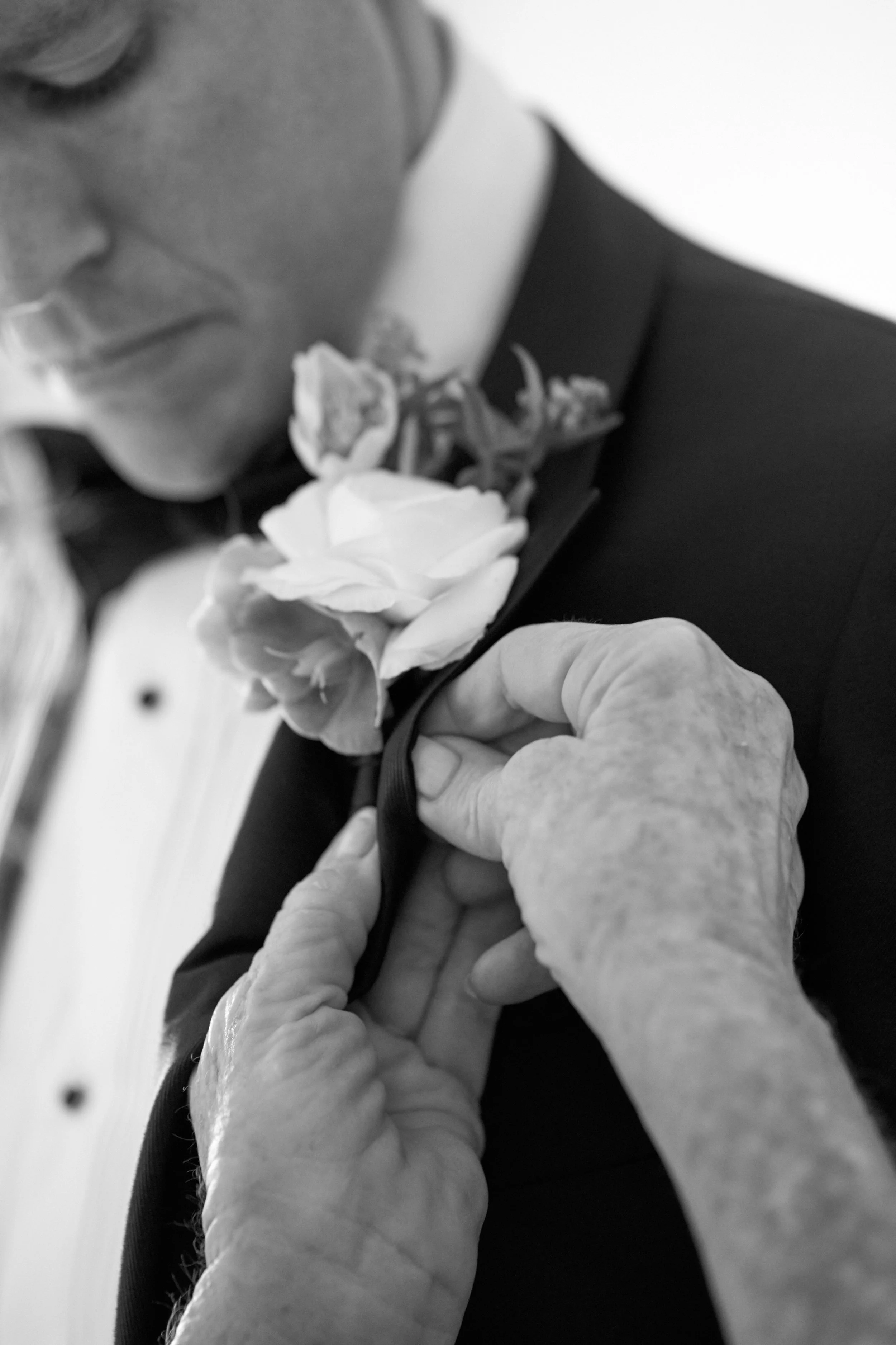 A person placing a flower on a person's suit lapel during a ceremony, captured in black and white.