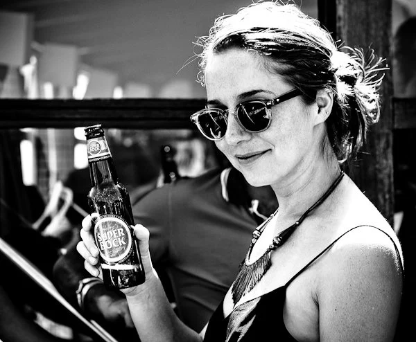Woman in sunglasses holding a bottle of beer at a social gathering.