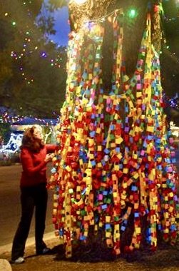 Kathleen Bethel stands near the Wishing Tree, which is decorated with multicolored paper wishes and holiday lights.