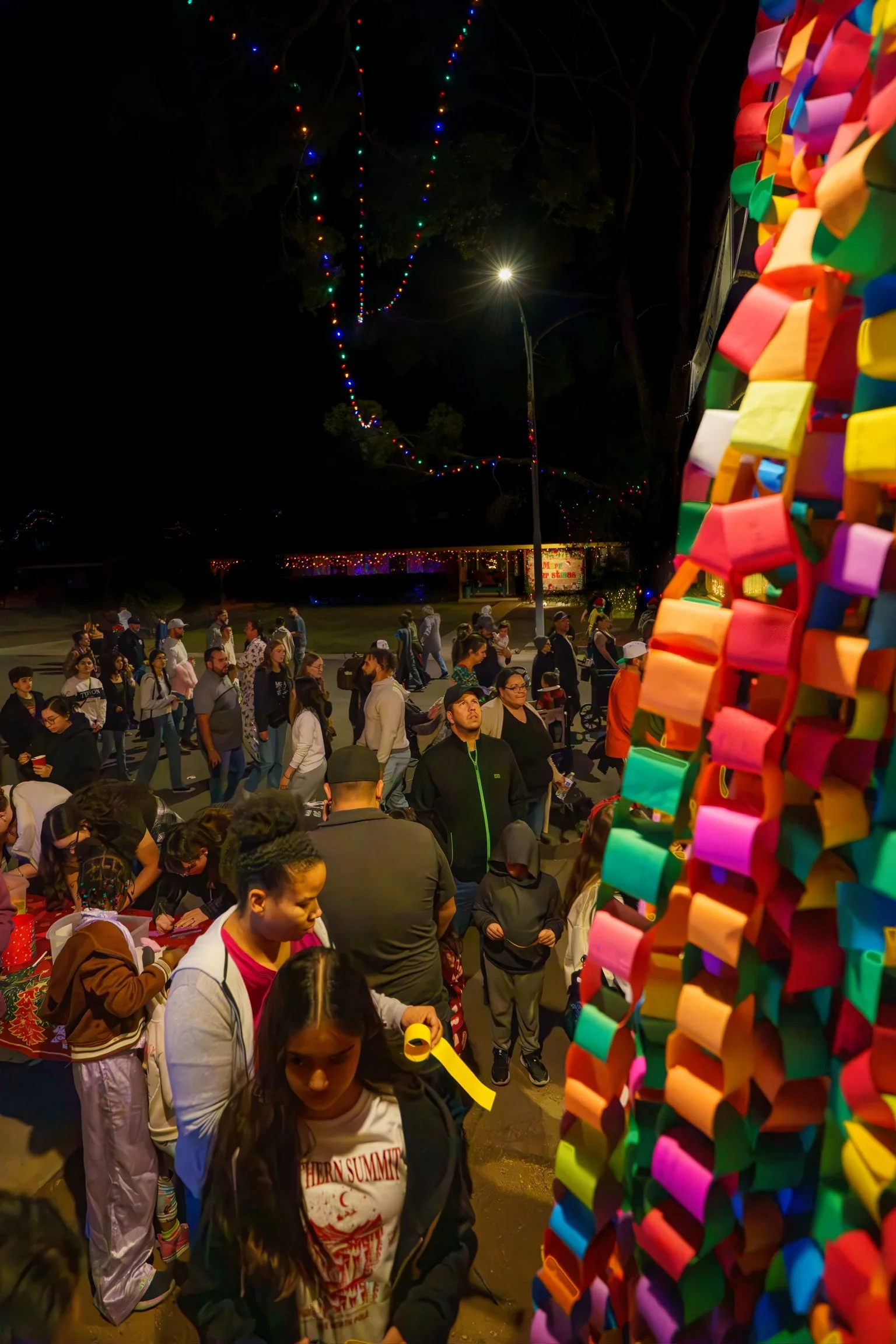 Nighttime scene at the home of Kathleen Bethel with people in line for the Wishing Tree, colorful decorations, and string lights overhead.