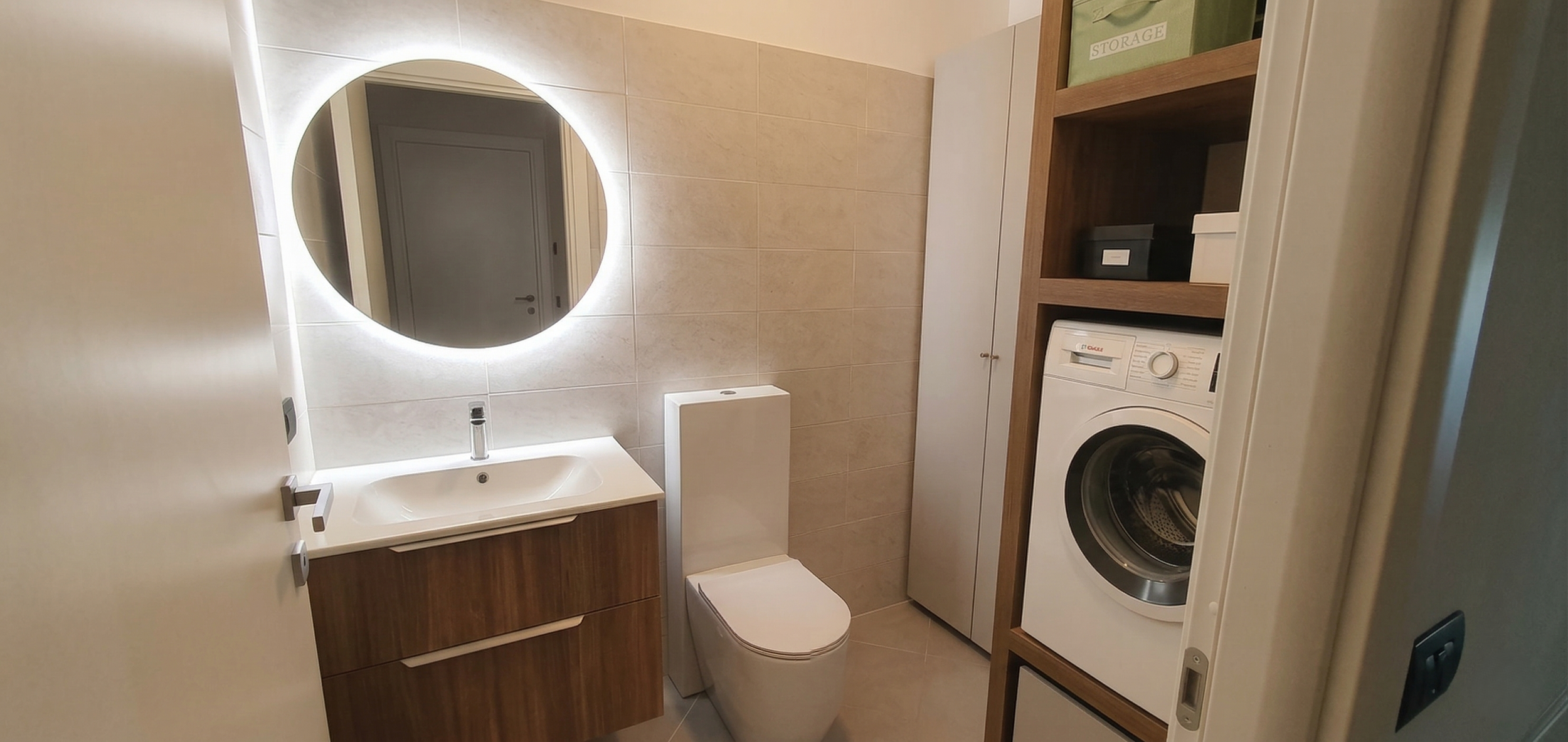 Bagno con lavabo, specchio rotondo con illuminazione, WC, armadio e lavatrice.