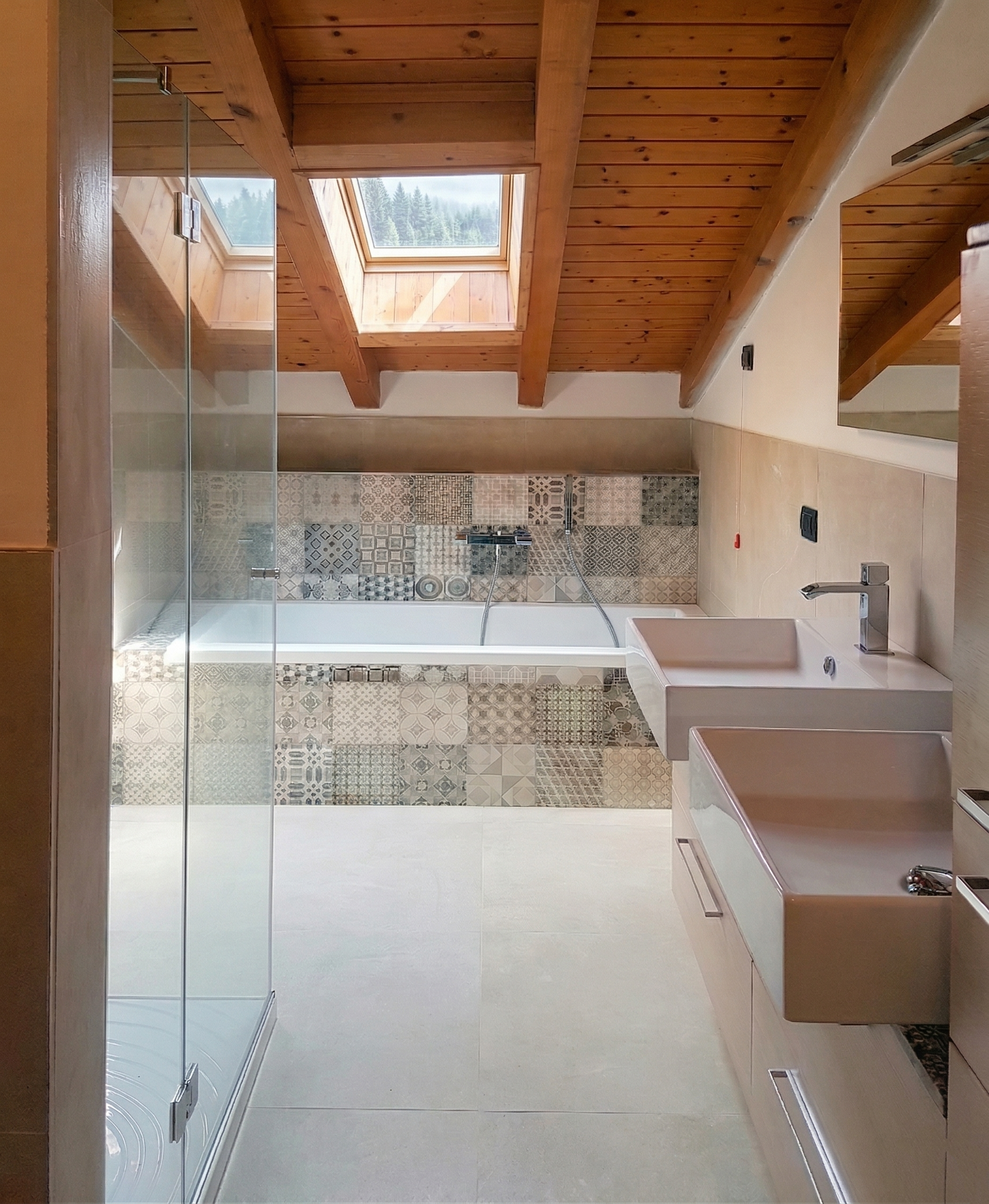 Bagno con doppi lavandini, vasca con piastrelle decorative sullo sfondo, soffitto in legno con lucernario.
