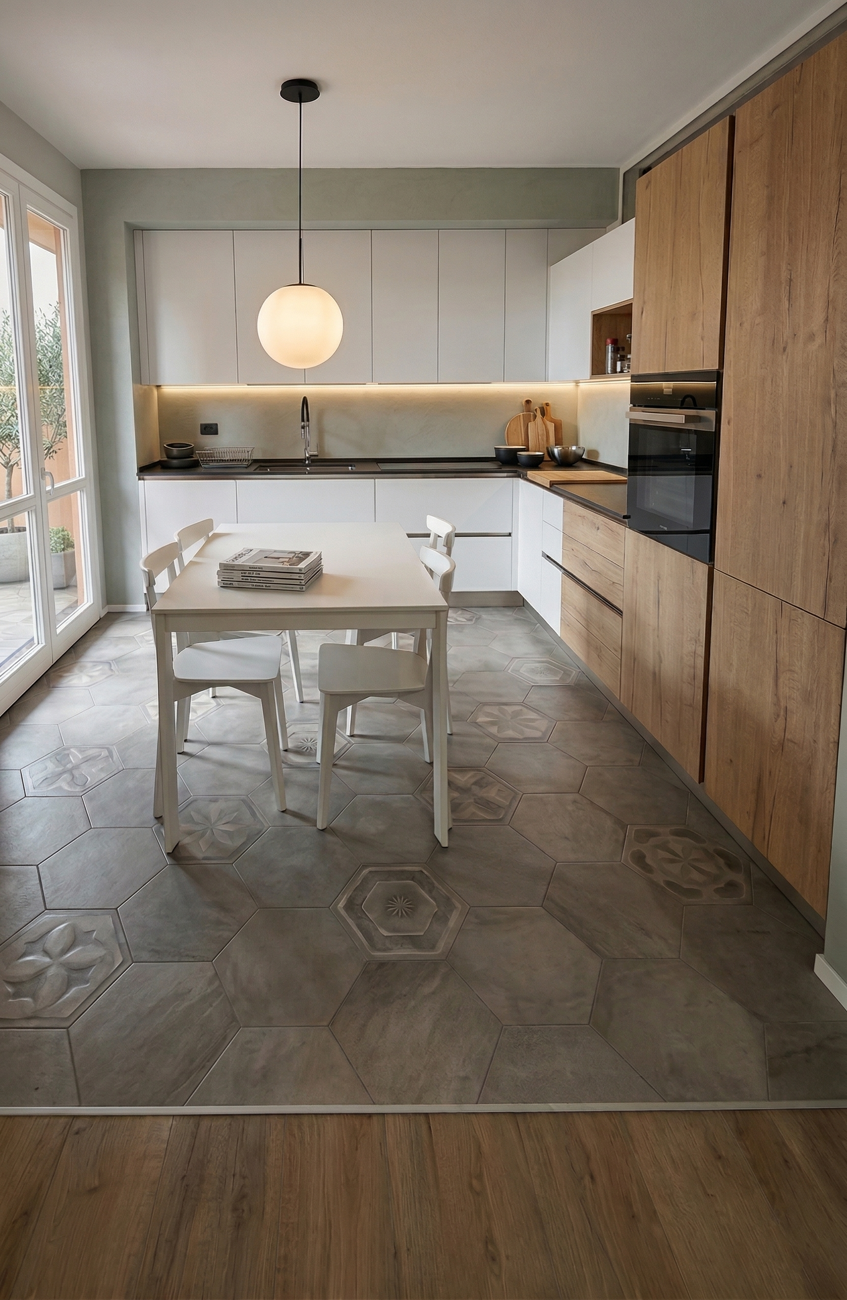 Cucina moderna con mobili in legno e pareti bianche, tavolo bianco con quattro sedie bianche, piastrelle decorative sul pavimento, lampada a soffitto e grande finestra sulla sinistra.