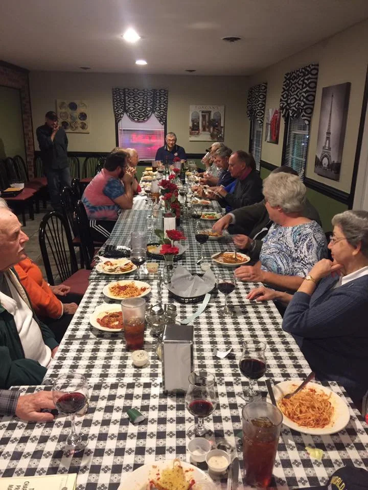 People gathered around a long dining table enjoying a meal and drinks inside a restaurant or banquet room.