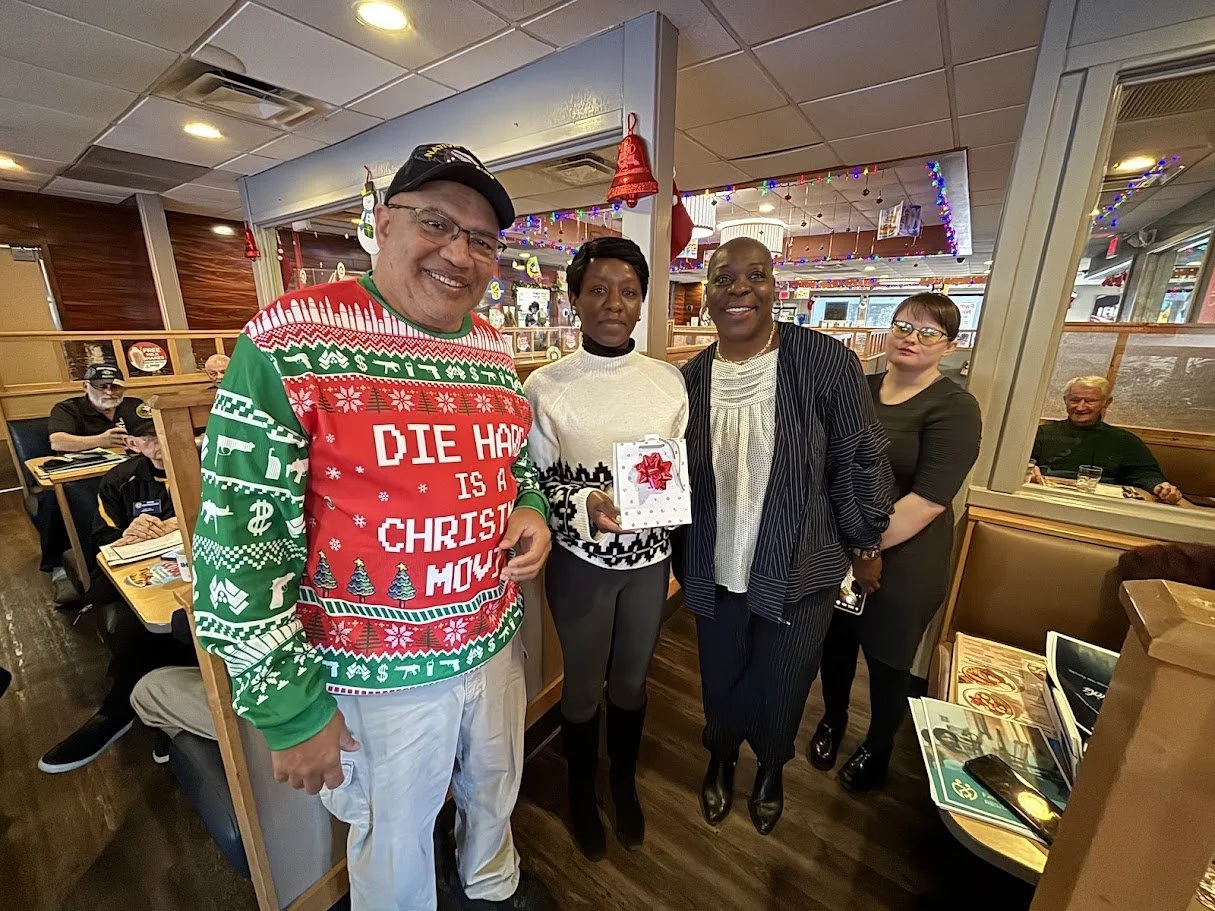 Group of people celebrating Christmas in a restaurant, with festive decorations and Christmas sweaters.