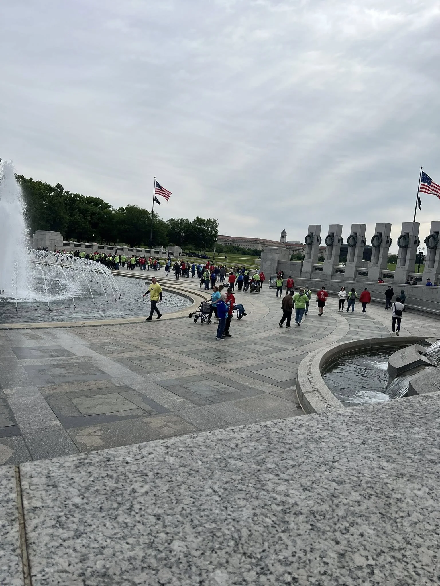People gathered at the Lincoln Memorial Reflecting Pool in Washington, D.C., with the memorial and American flags in the background, and a fountain in the foreground.