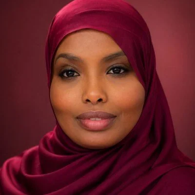 Portrait of a woman wearing a burgundy headscarf against a matching background.