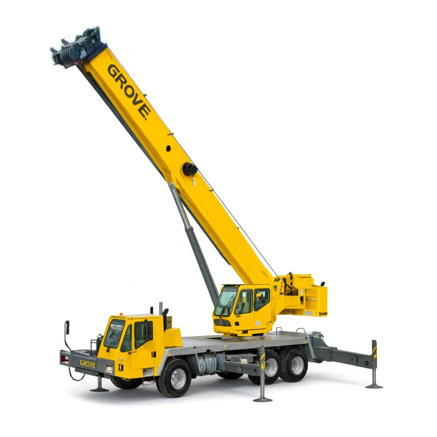 A yellow crane truck parked on a gravel lot with palm trees and other greenery in the background, partly cloudy sky overhead.