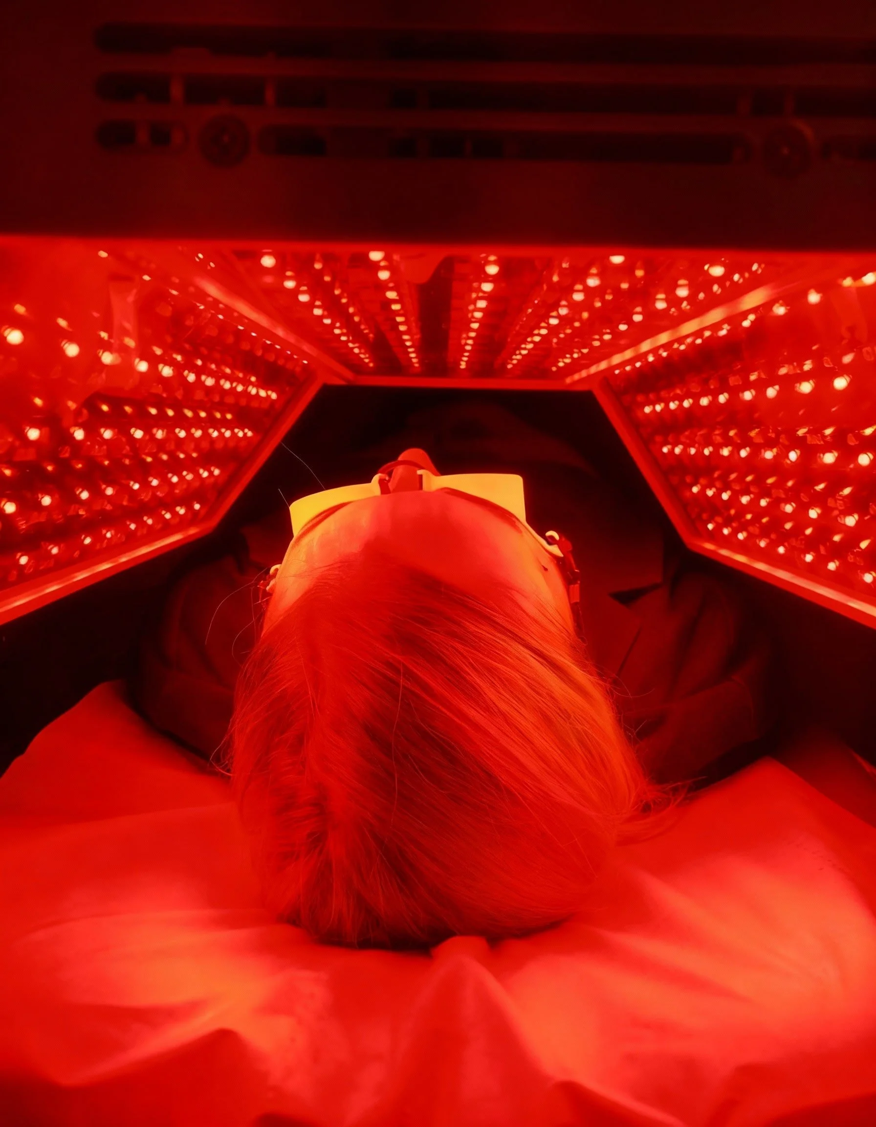 Une personne allongée sous une cabine de luminothérapie rouge, portant des lunettes de protection.