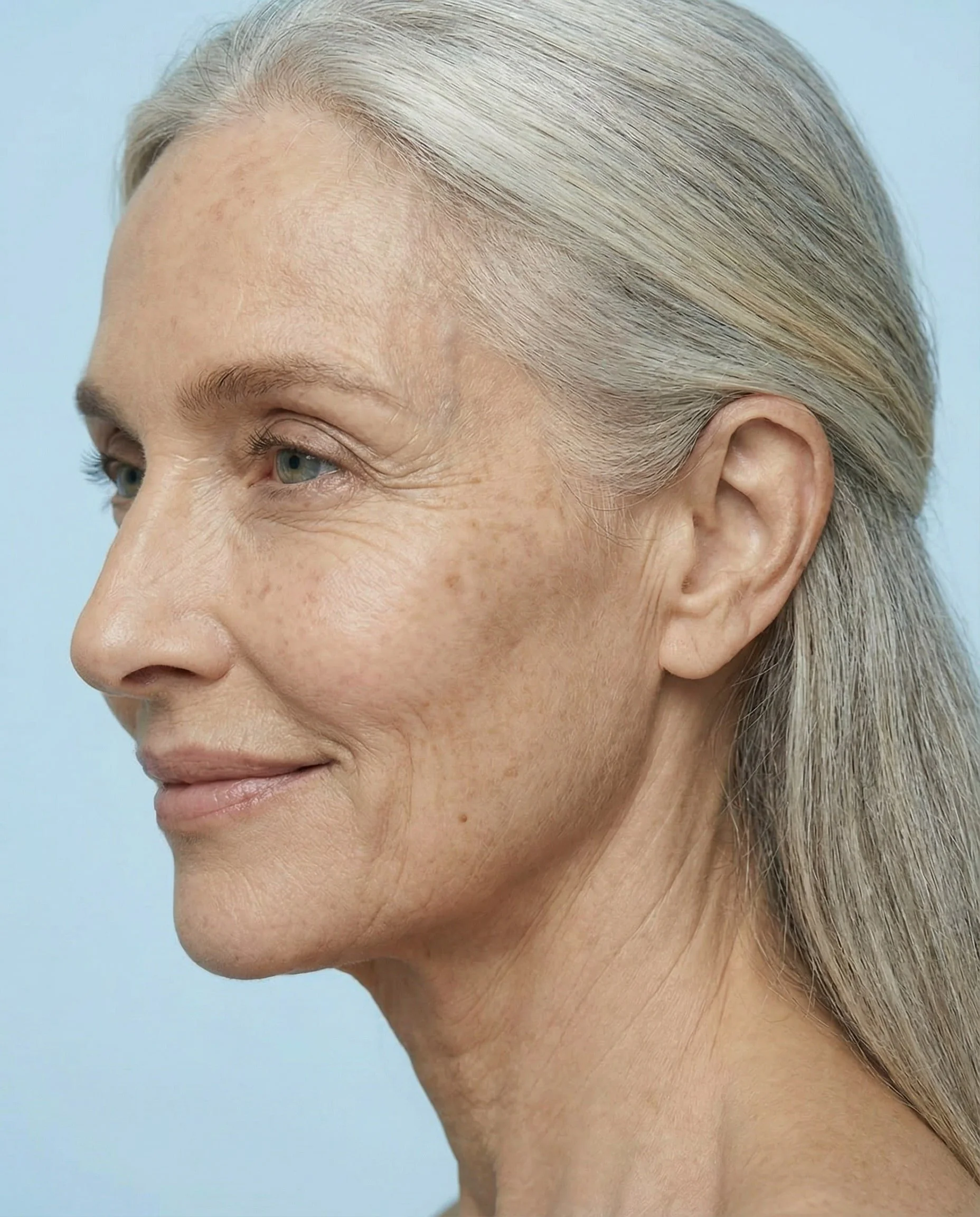 Profil d'une femme âgée avec cheveux gris tirés en arrière, peau claire, souriant doucement, rides légères.
